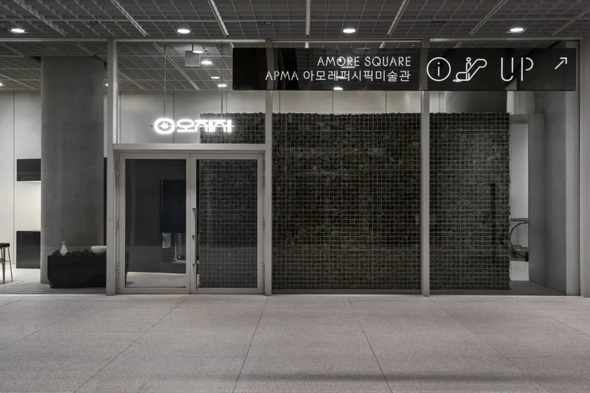 現代購物中心外觀，配備大型玻璃牆、黑色磚片點綴，以及前方置有長椅