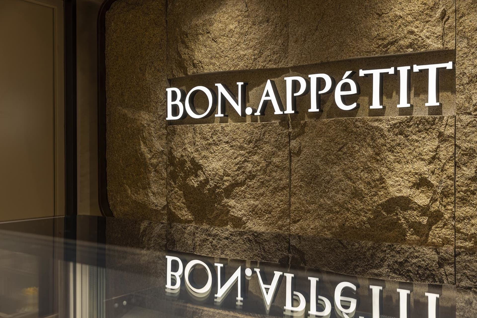 A restaurant interior with a stone wall and a sign reading Bon Appetit, creating a warm and inviting atmosphere