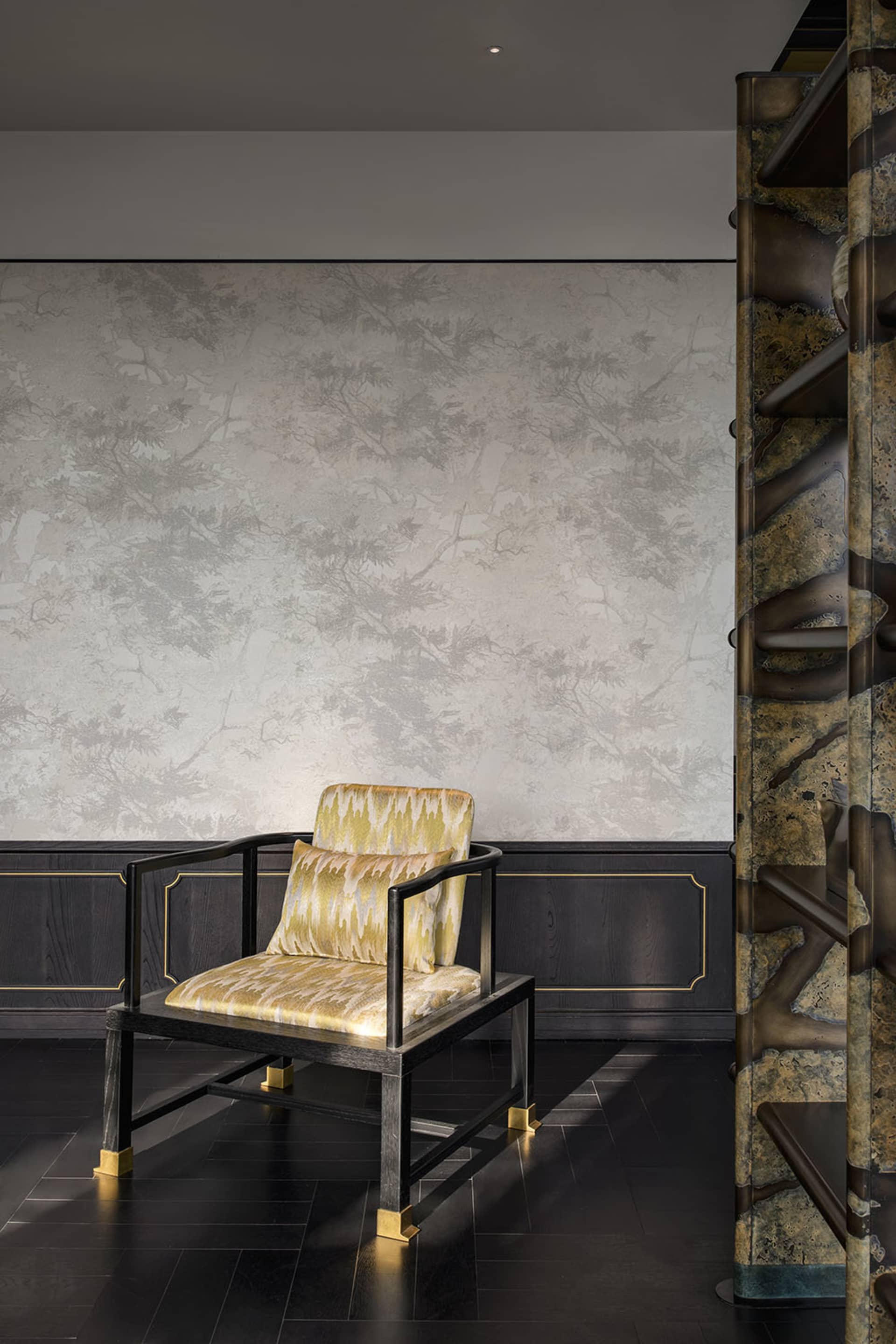A cozy living space with a chair in front of a wall featuring a patterned wallpaper, with a wooden chair and yellow and black striped upholstery