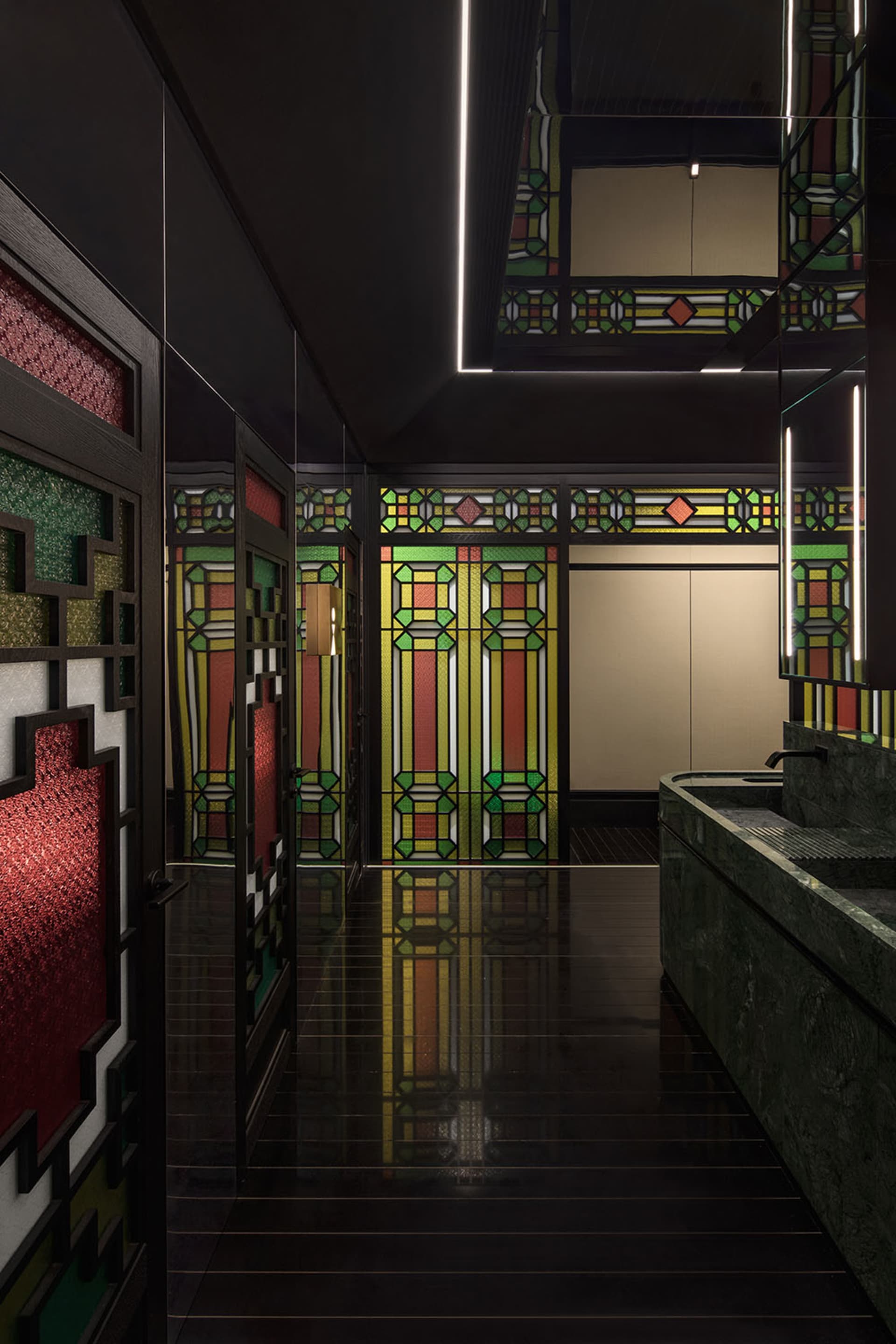 Ornate bathroom with green tiles, red accents, a large mirror above a sink, and two doors