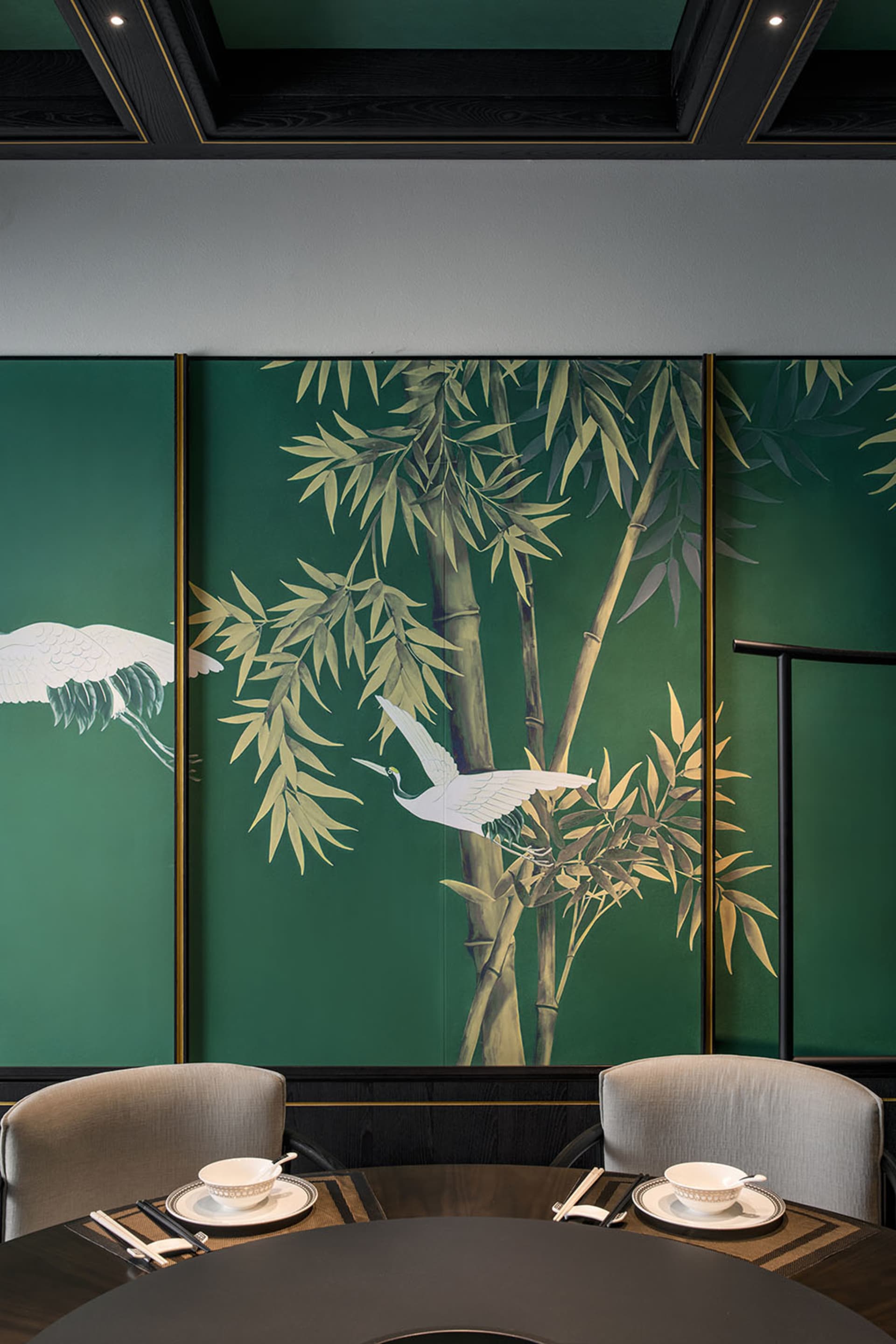 Serene living space with green walls, artwork of birds on bamboo trees, and two chairs in a calming environment