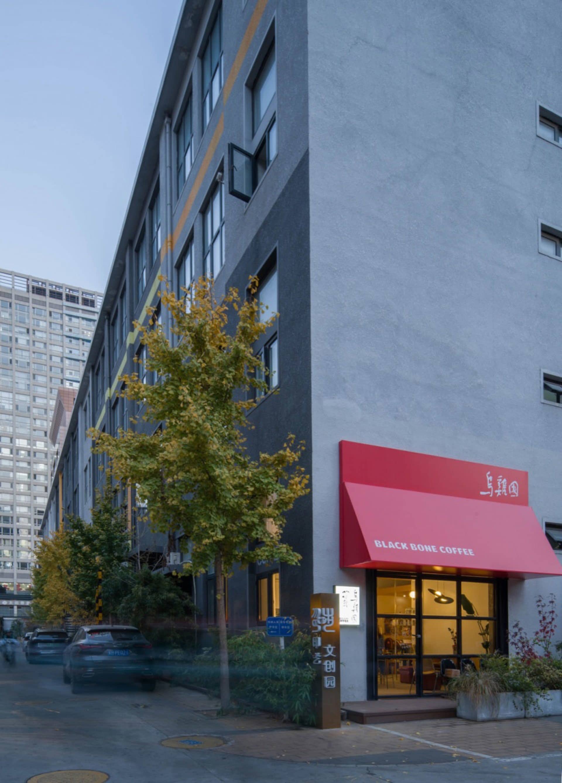 A city street view of a building with a red awning, windows, and a tree, with cars parked nearby