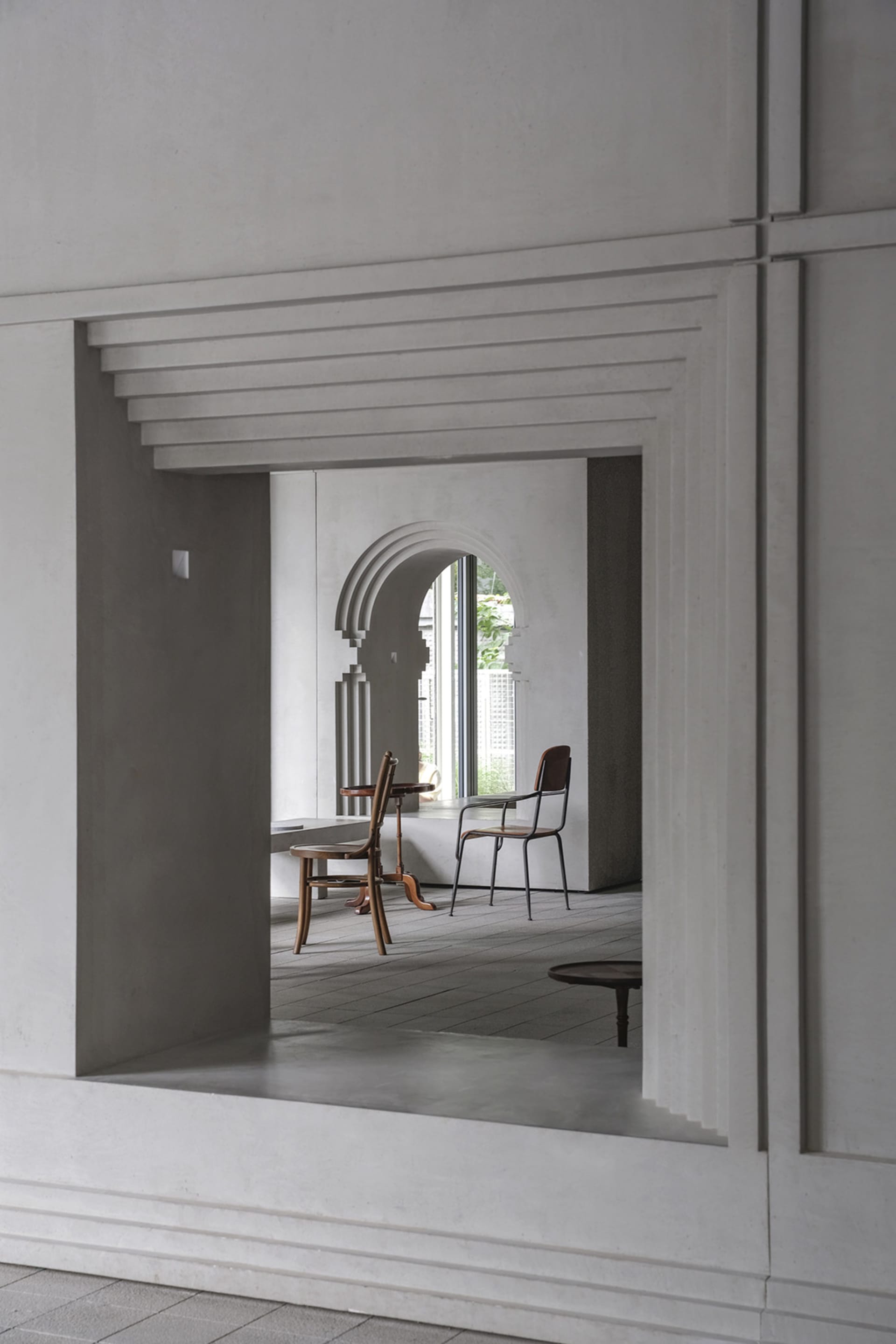Empty living area with a white wall, a doorway, two chairs, and a table, creating a calm and minimalistic atmosphere