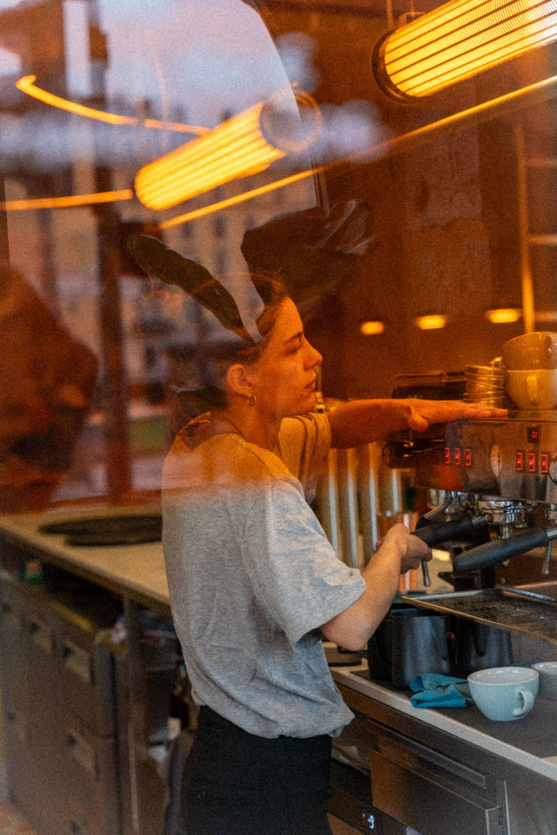 A woman prepares coffee in a casual kitchen with a sink, dining table, and various cups, set in a comfortable atmosphere