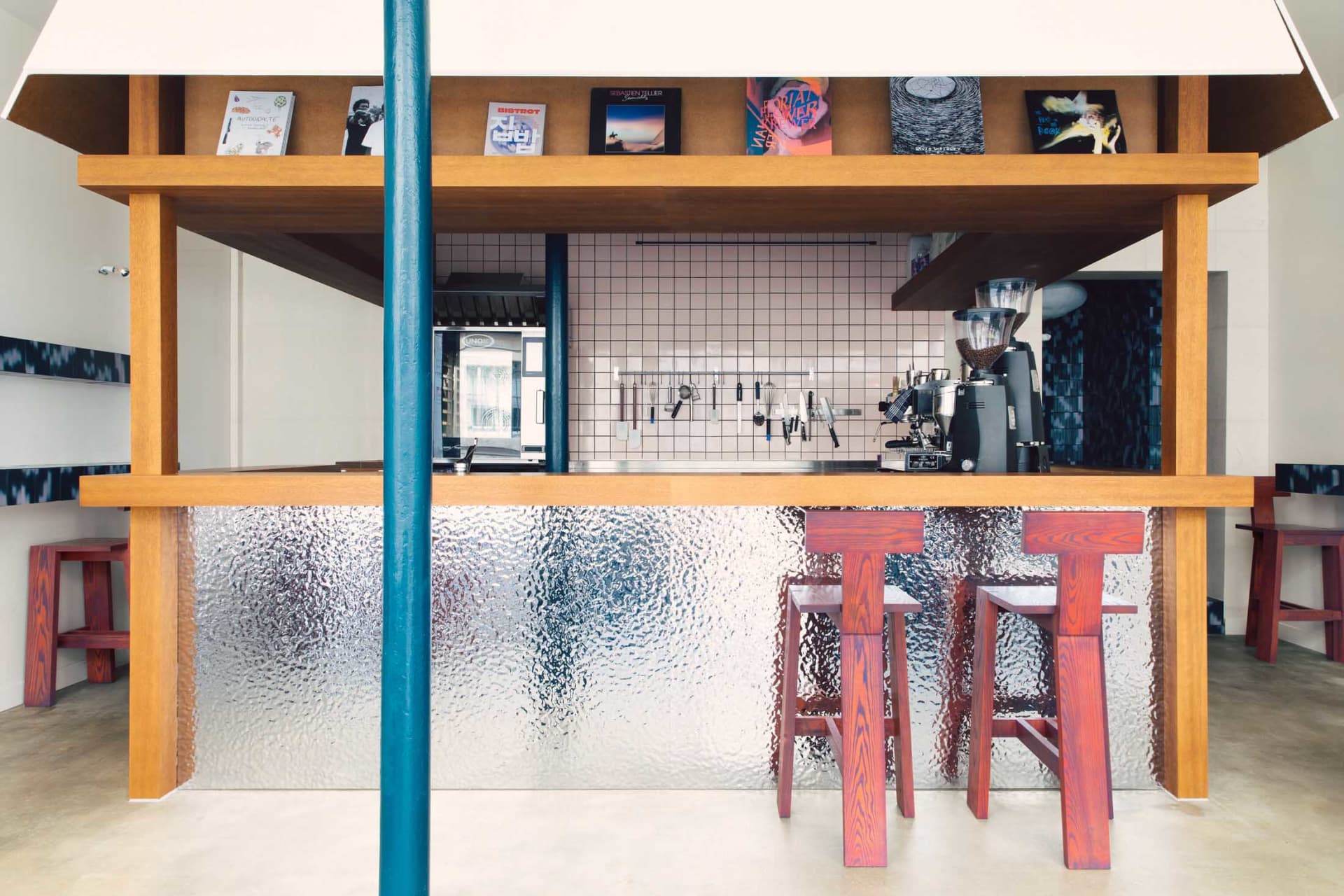 Cozy modern kitchen with wooden floors, walls, and a counter with stools and a coffee maker, surrounded by scattered books