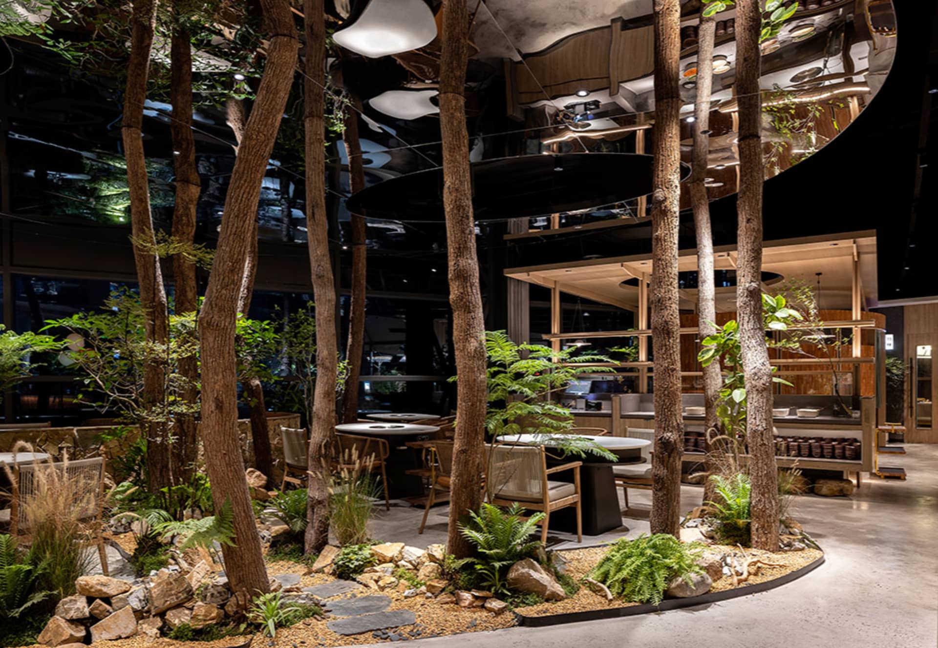 Modern restaurant interior with wood and stone elements, surrounded by trees, and featuring dining tables, chairs, and potted plants