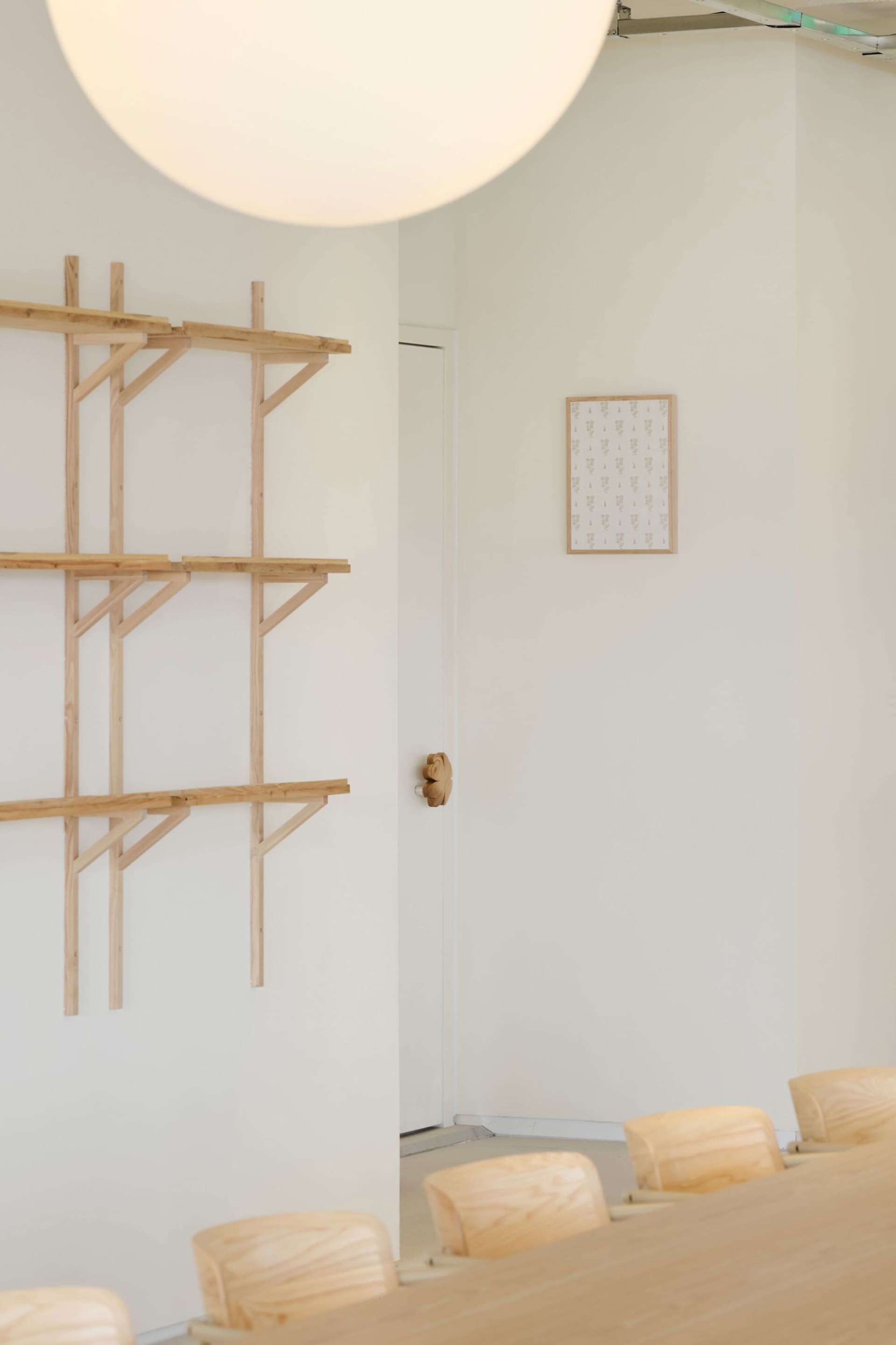 A clean and organized interior space with a white wall and three wooden shelves of varying heights, creating a minimalist atmosphere