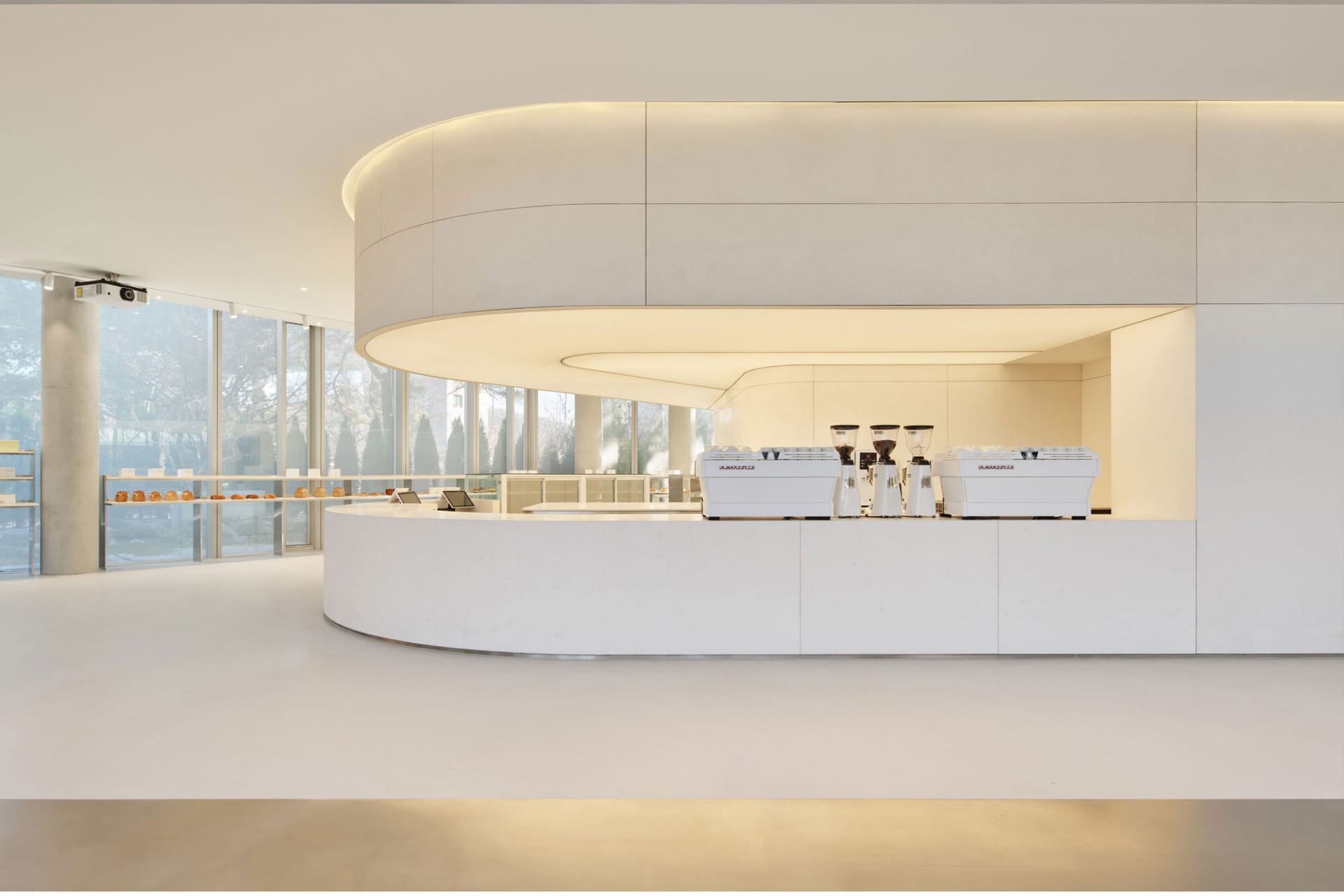 Open kitchen with white walls and countertops, featuring two coffee machines and scattered cups, conveying a clean and organized atmosphere with a focus on functionality