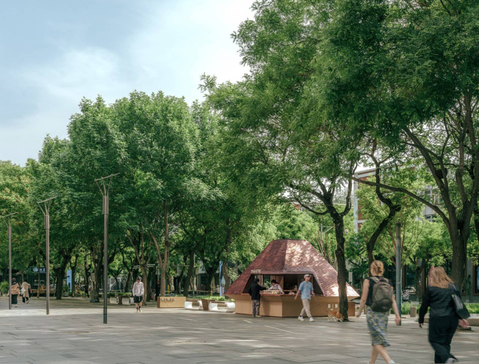 A public plaza with a small food stand and several people walking around, surrounded by benches and outdoor seating areas