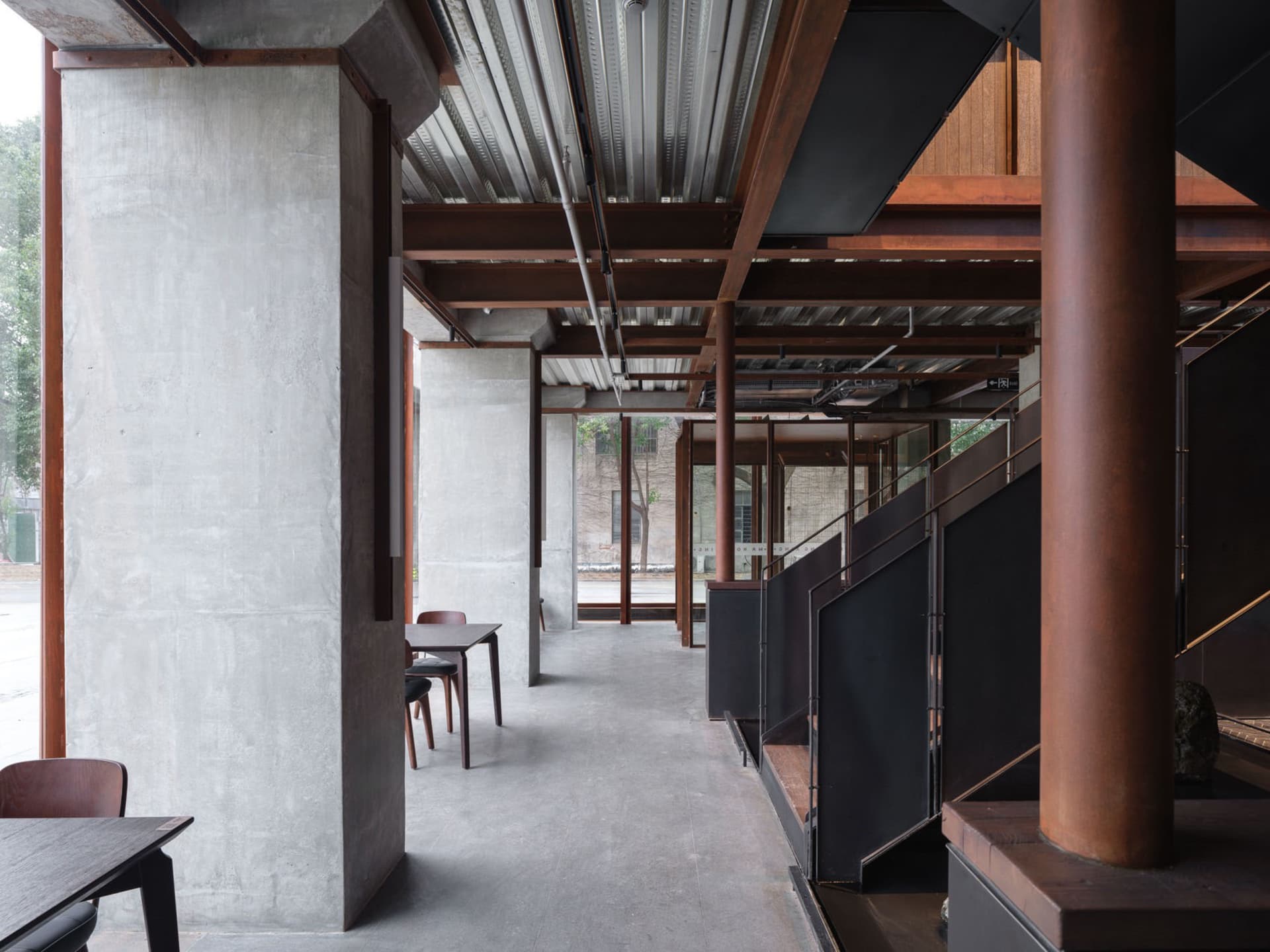 A modern building with concrete walls and floors, featuring multiple rooms, staircases, and chairs, conveying a sense of spaciousness and functionality