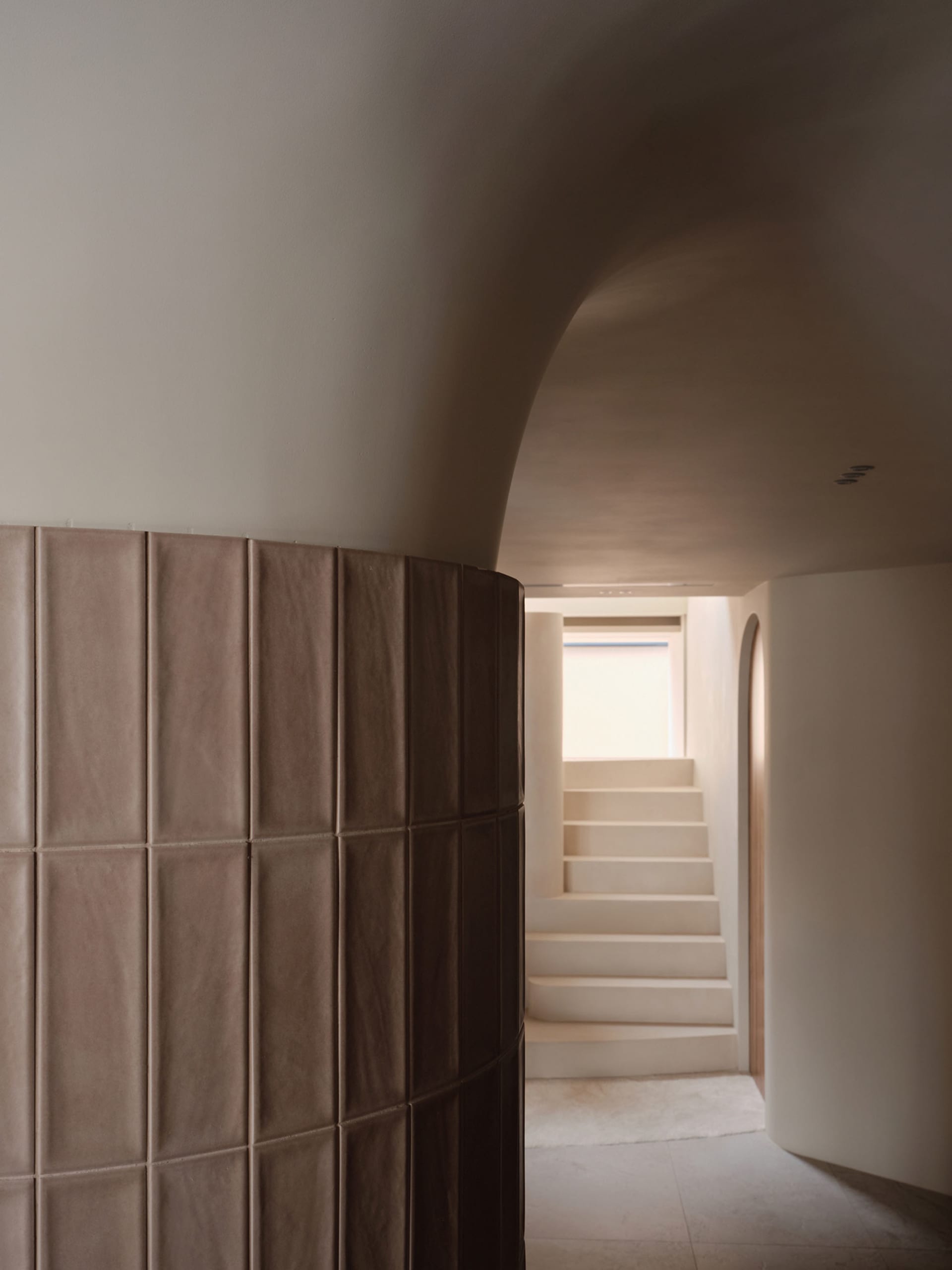 A dimly lit interior stairwell with concrete stairs and tiled walls, conveying a sense of depth and complexity