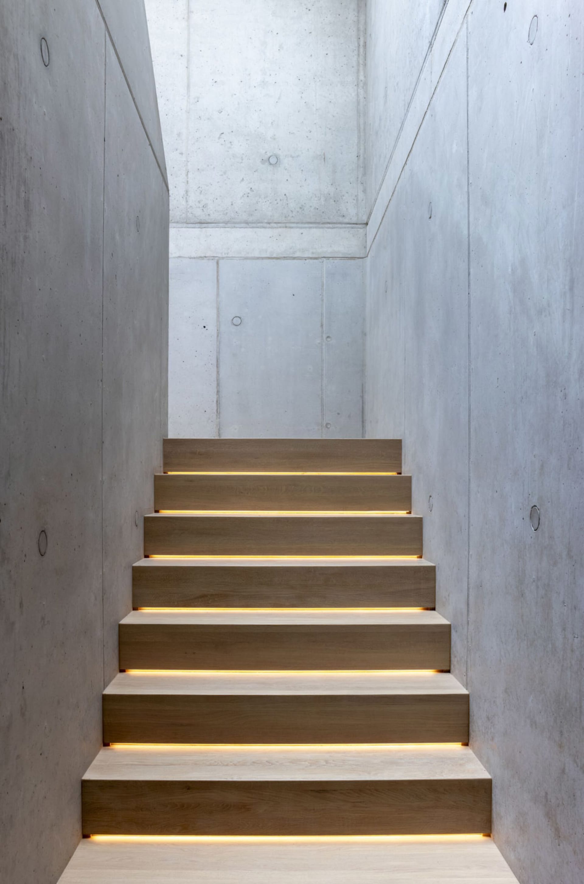 A well-lit stairwell in a building with concrete walls and steps, illuminated by lights on each step