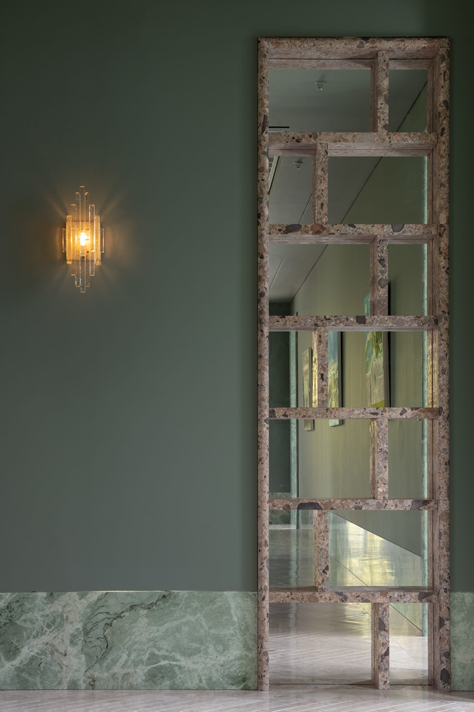 A room with a large mirror mounted on a wall, reflecting a green accent wall and other interior design elements