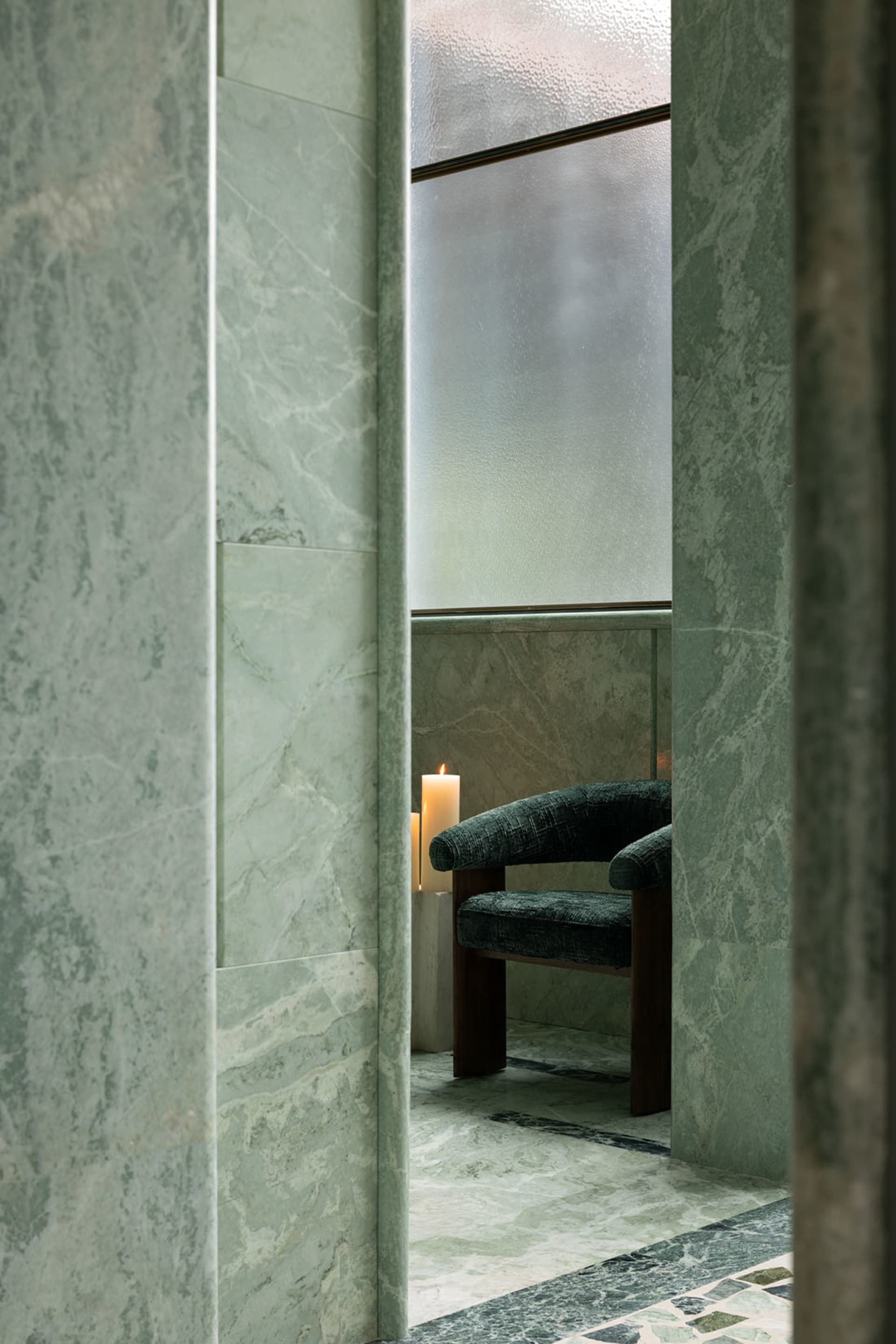 Bathroom with a shower stall containing a wooden chair with a black seat and two candles on the floor for a cozy ambiance