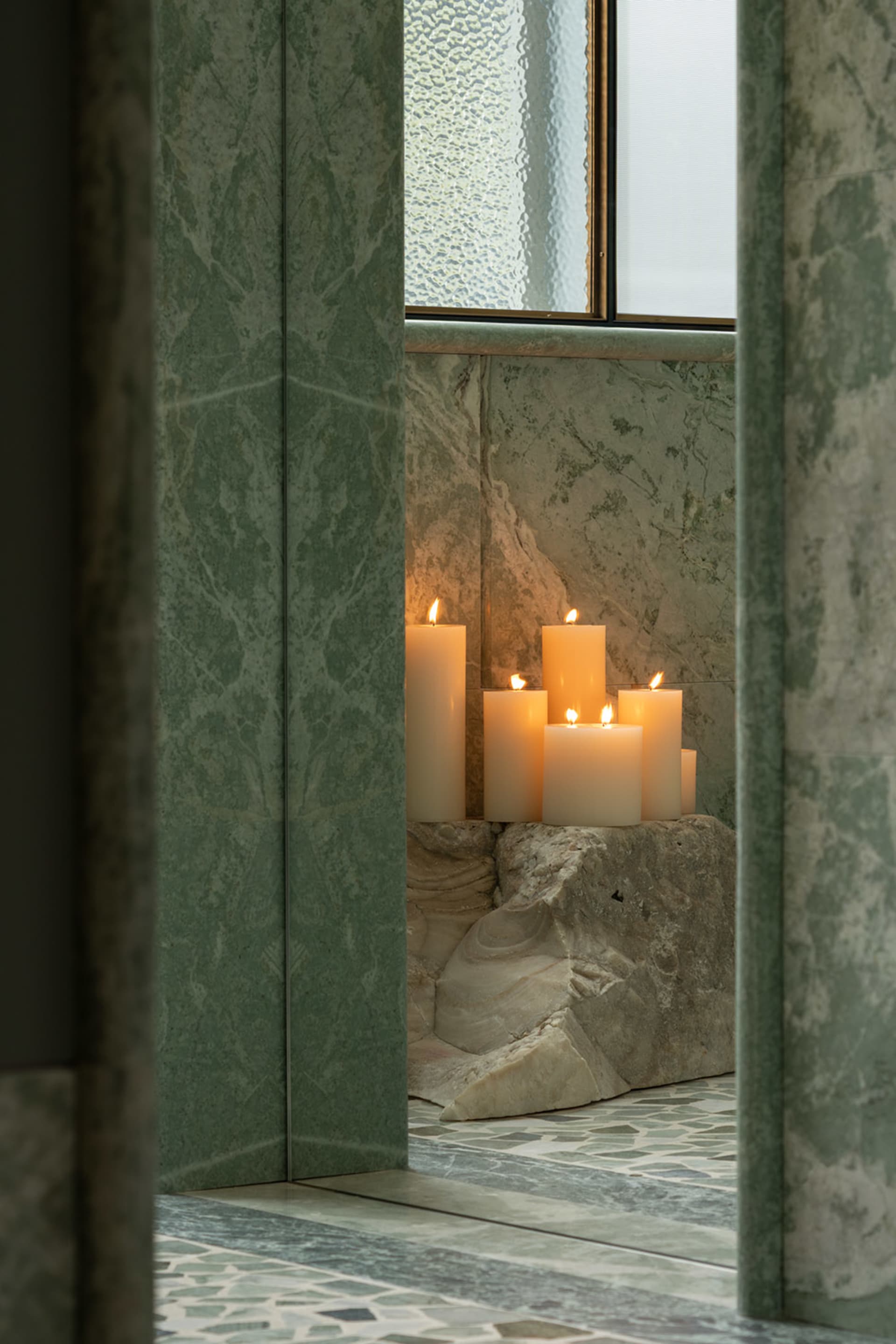 Bathroom scene with a marble wall featuring three lit candles, creating a warm and relaxing ambiance