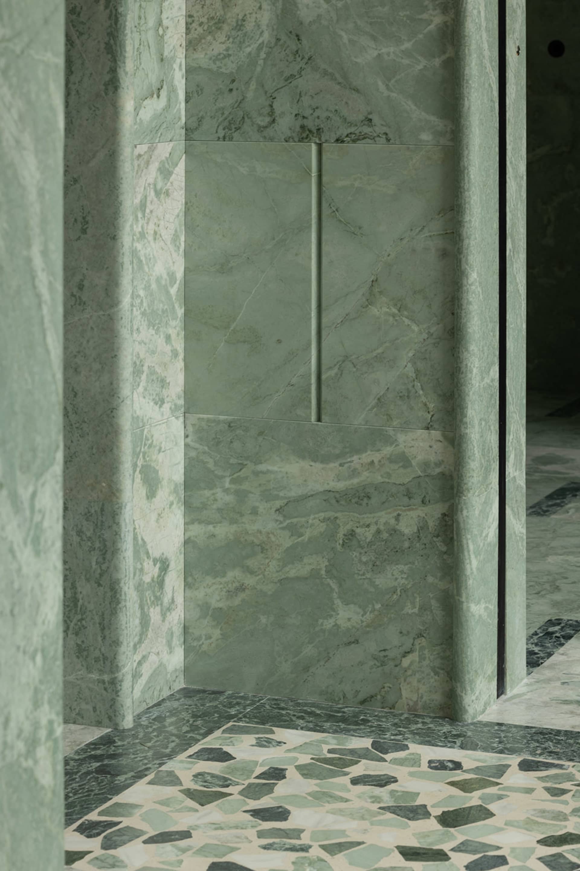 Bathroom with a green-tinted marble wall, two doors, and a sink, showcasing a well-designed space with a distinctive feature