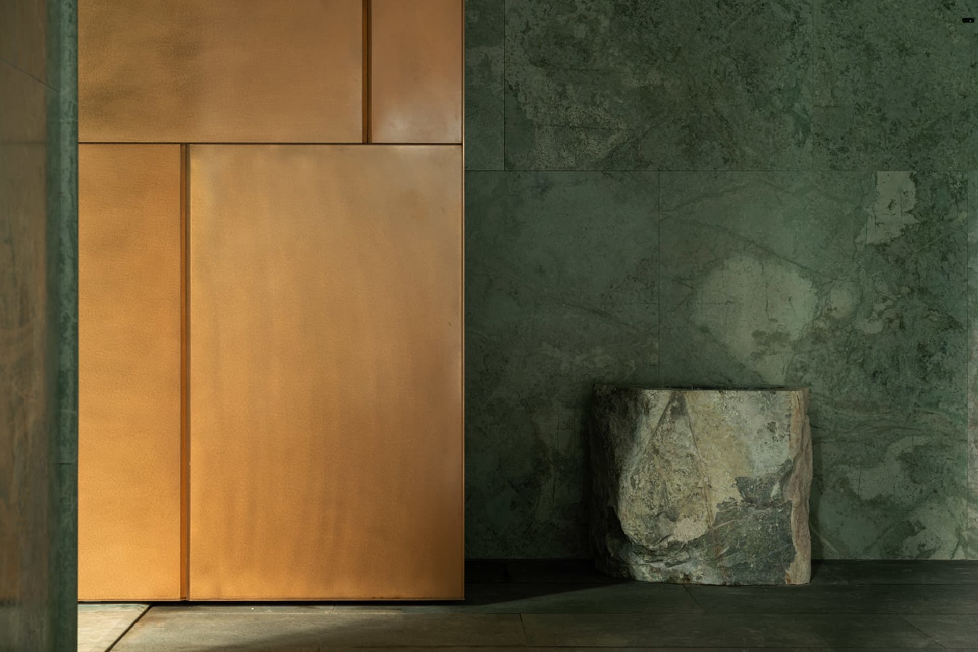 A spacious entryway with a large brown door featuring a gold metal finish, situated in front of a green-tinted wall, with two additional doors on either side and a rock in the center