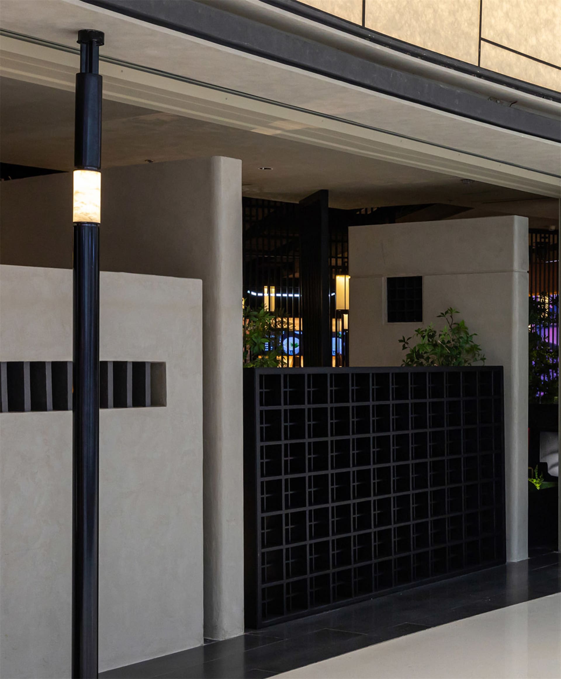 A modern indoor space with a metal pole supporting a street lamp, surrounded by potted plants and minimalist decor