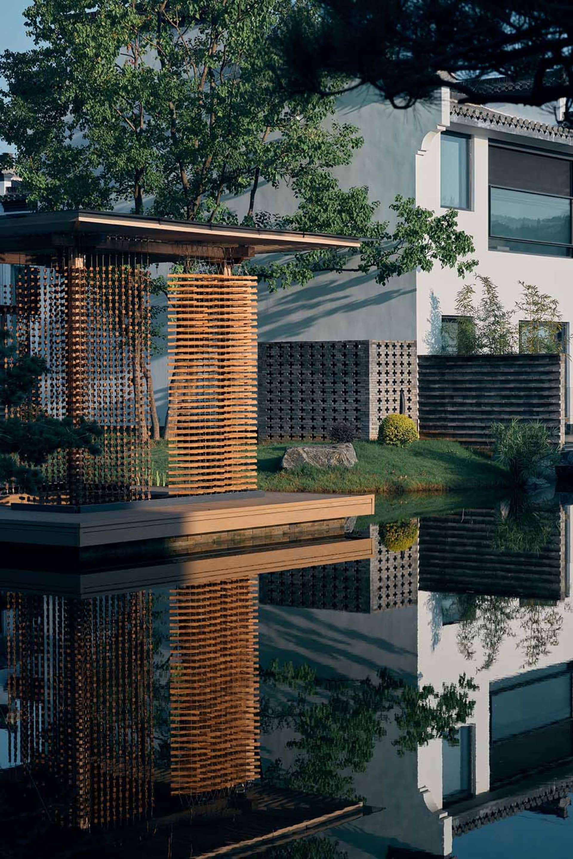 A large white house with a modern design, surrounded by trees and a pond, creating a serene atmosphere