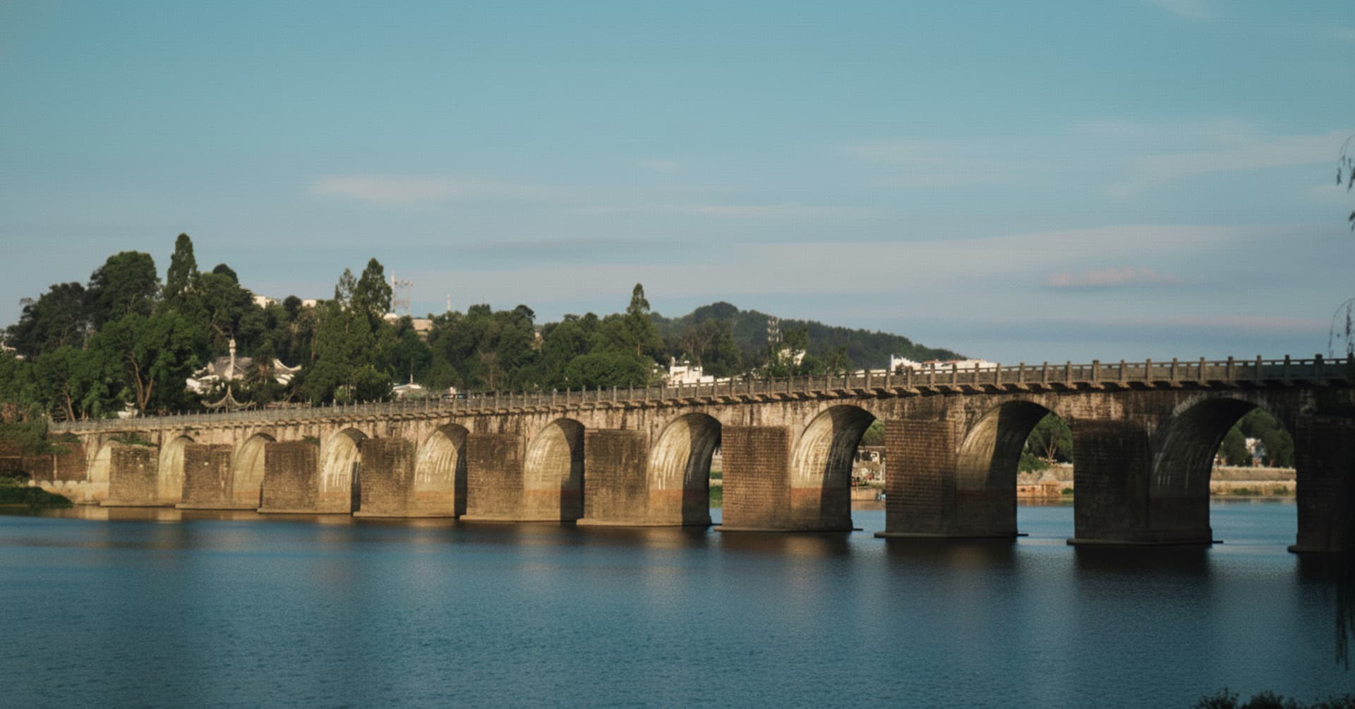 A serene stone bridge with arches spanning across a calm body of water, reflecting the bridge's presence