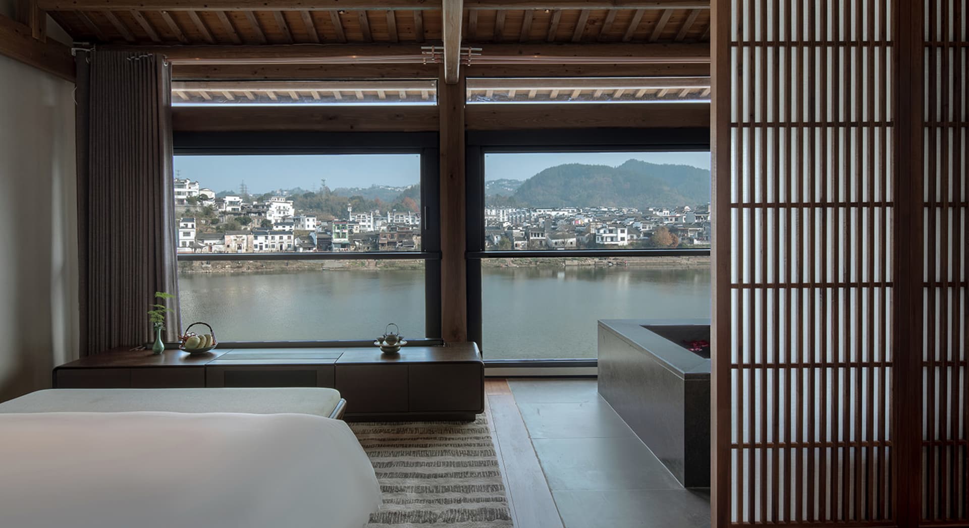 Open modern living area with wooden elements, a large window overlooking a river, and a serene atmosphere