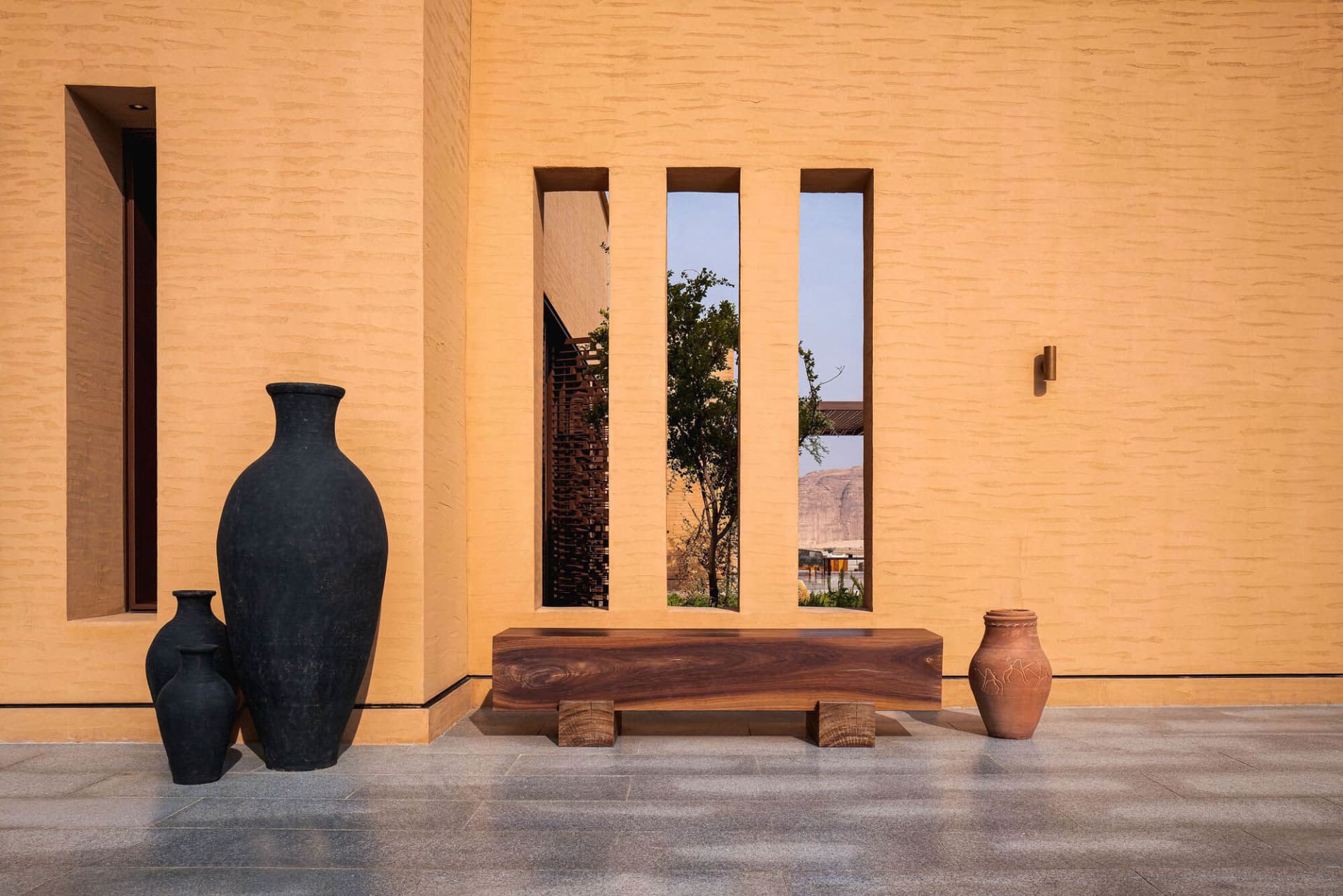 A residential or commercial space with a wooden bench in front of a window, surrounded by vases and natural light