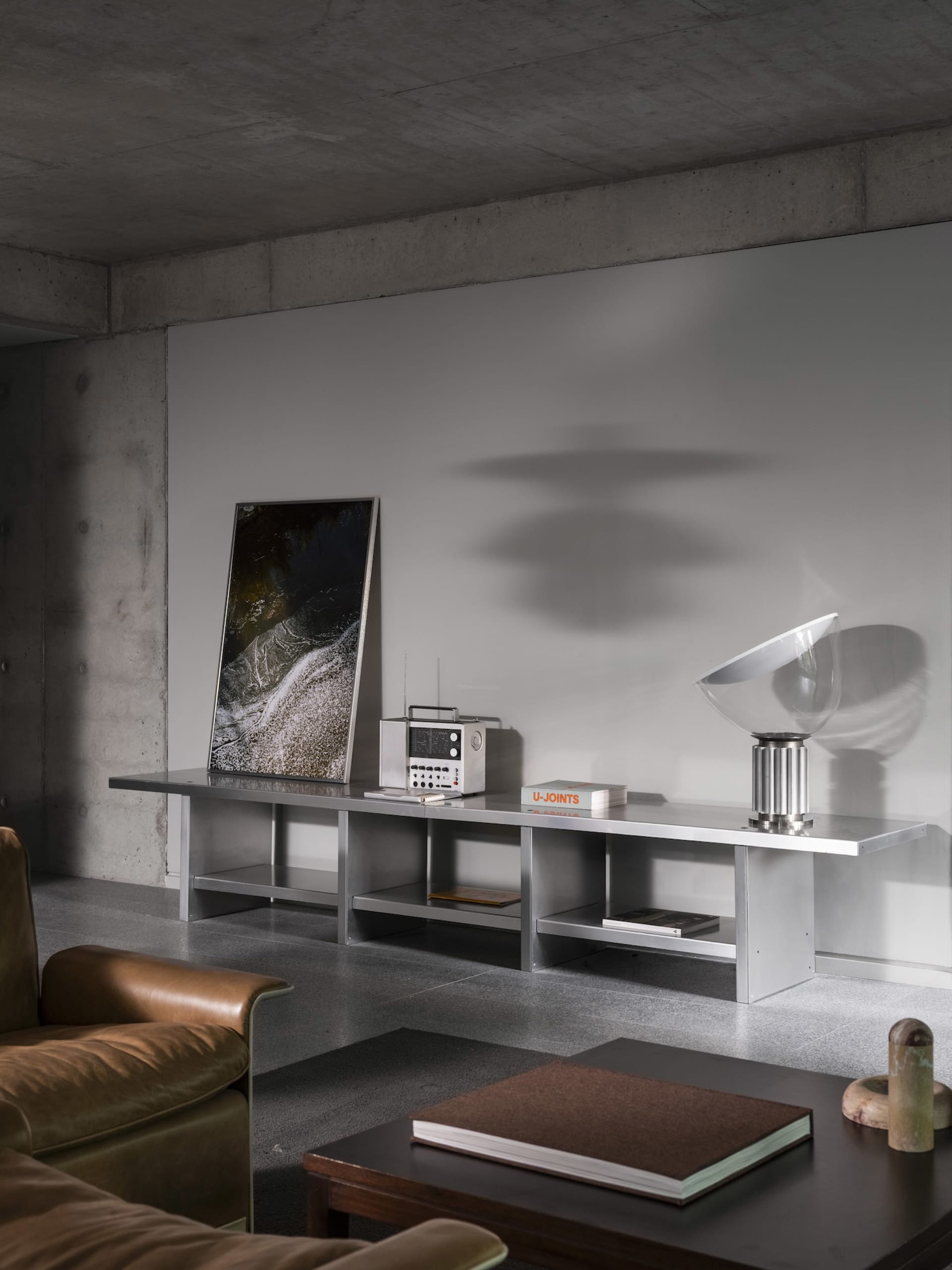 Modern living room with a couch, chair, and dining table, featuring grey walls and a concrete floor, with various pieces of furniture and decorative items