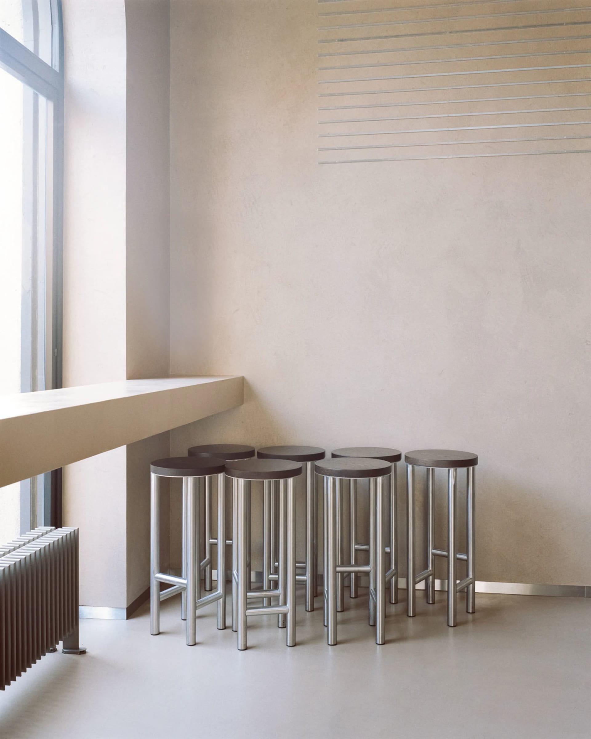 Empty room with four metal stools in the center, surrounded by white walls and a minimalist design, creating a calm and inviting atmosphere