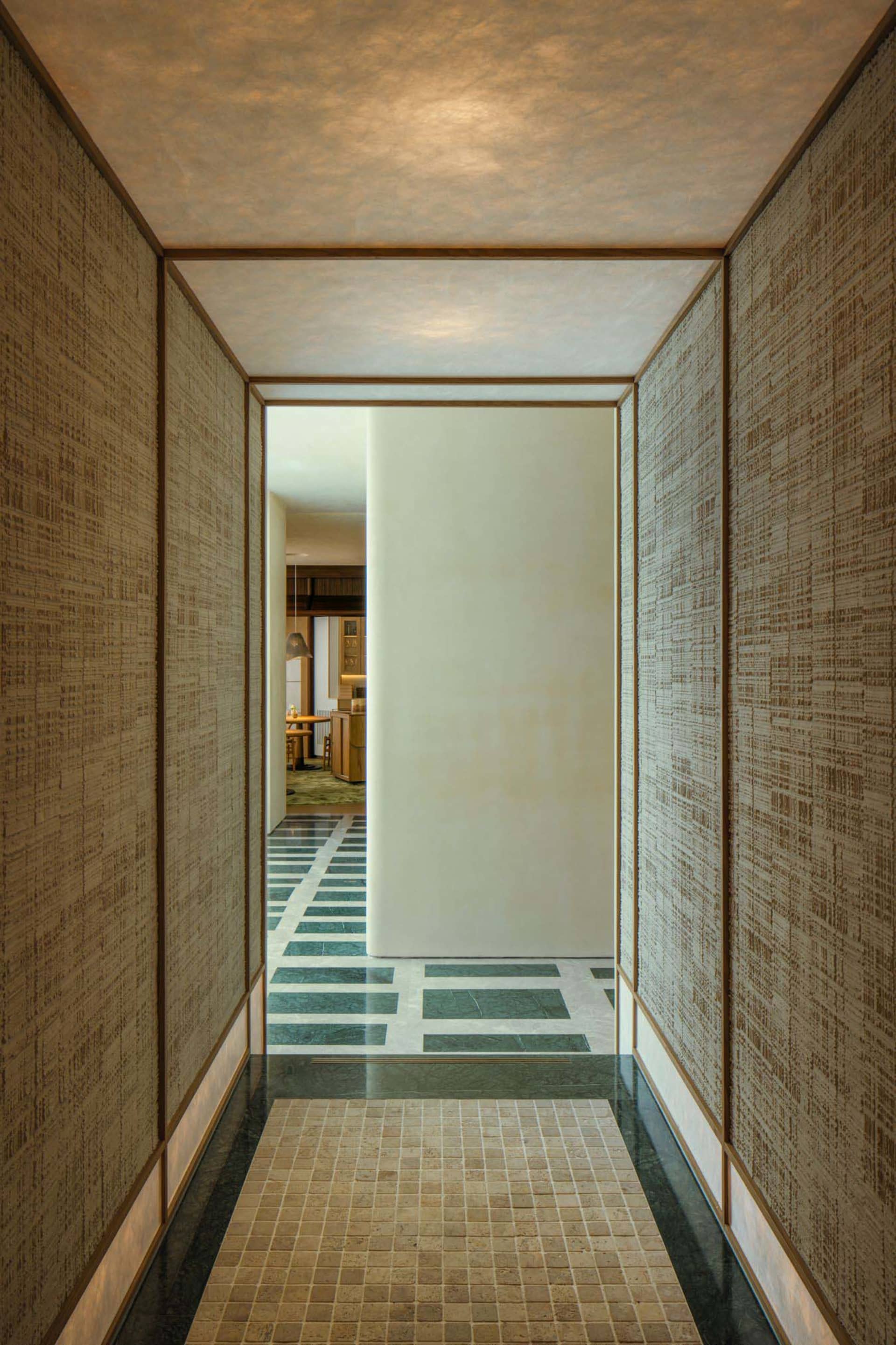 A well-lit hallway with a white wall and brown tiles, featuring two doors and a bright atmosphere