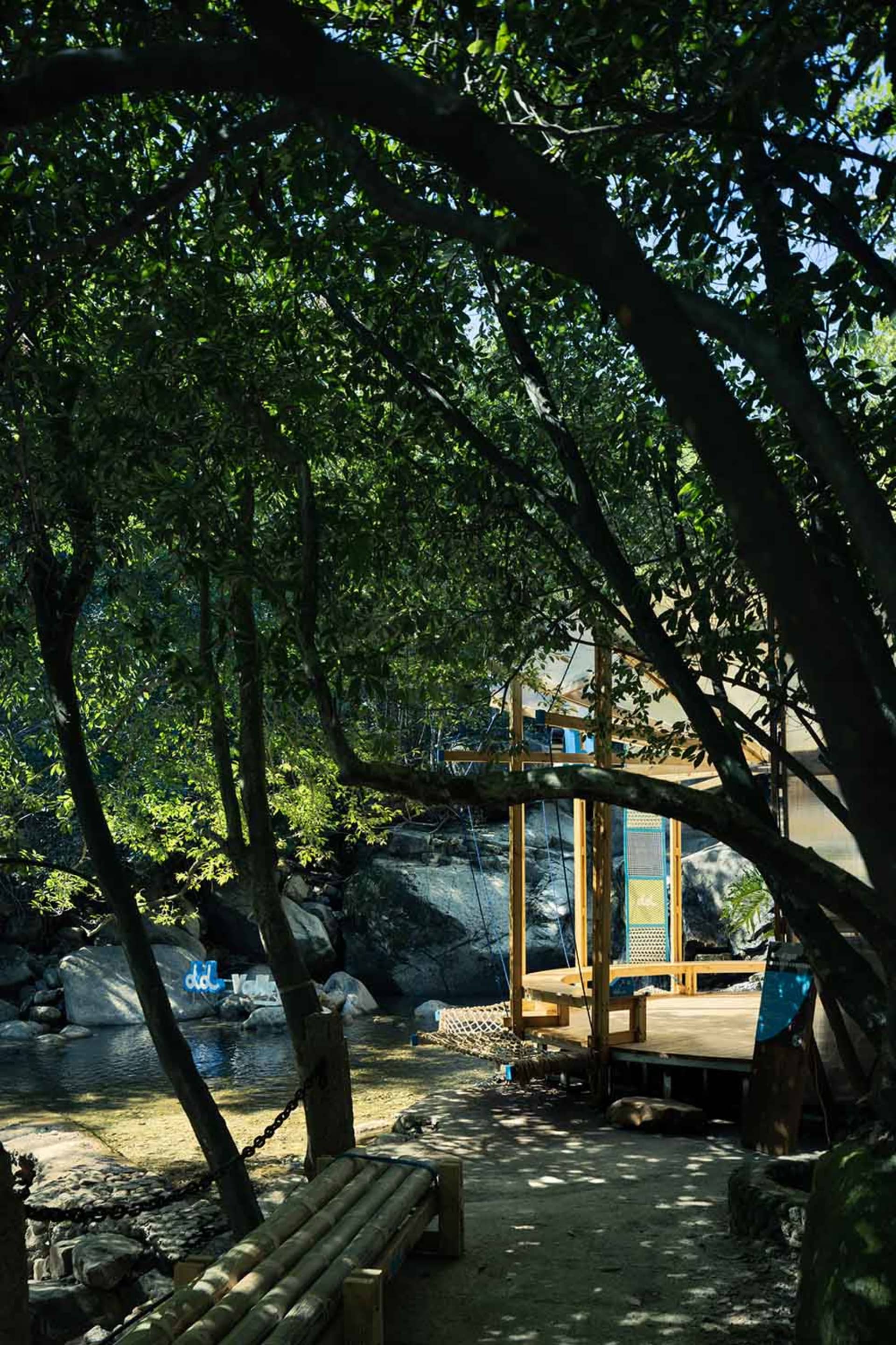 A real photo of a house with a wooden deck overlooking a river, surrounded by trees, with a bench for relaxation