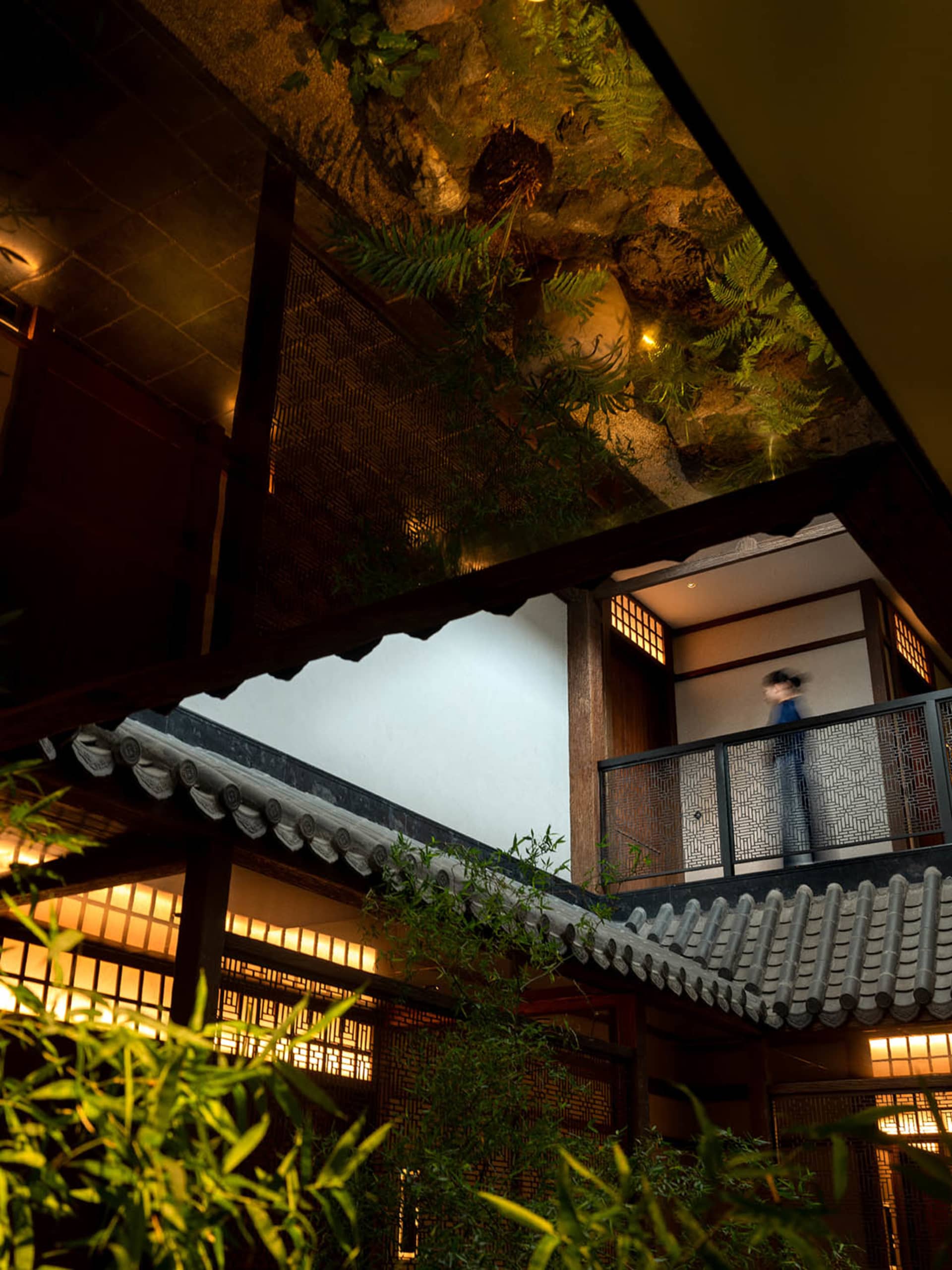 A traditional Asian building with a staircase leading to a balcony, featuring a person walking up the stairs and another person standing nearby