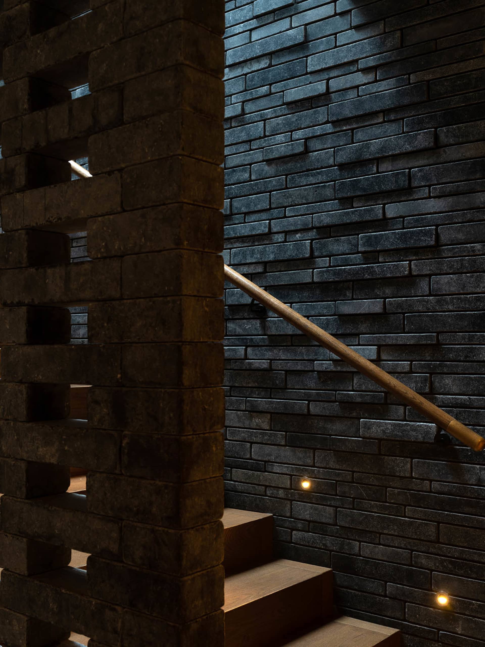 A classic interior stairwell with a brick wall, wooden railing, and stone stairs, evoking a sense of history and timelessness