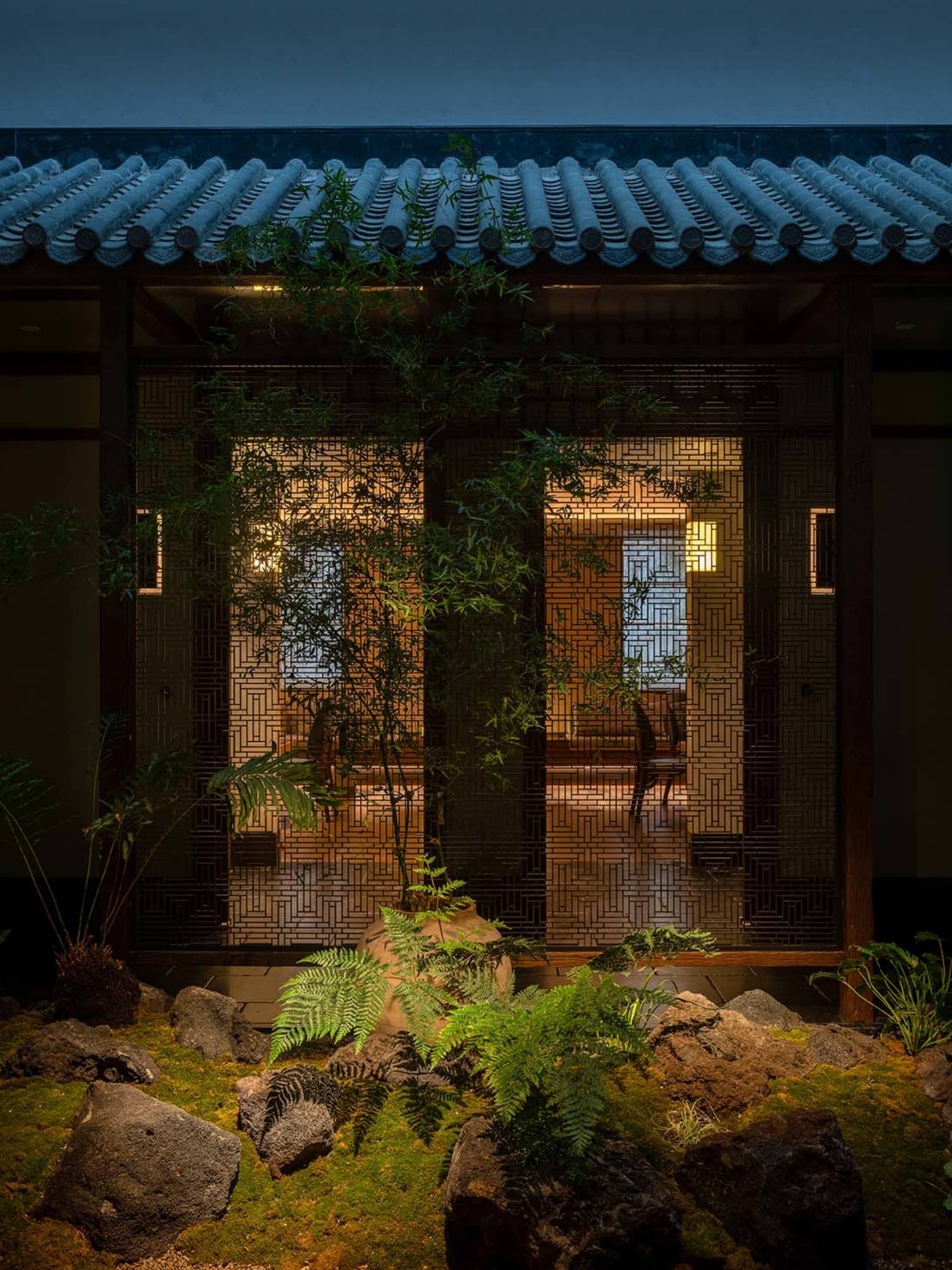 Asian-style house with a tile roof, two doors, potted plants, and chairs in a courtyard