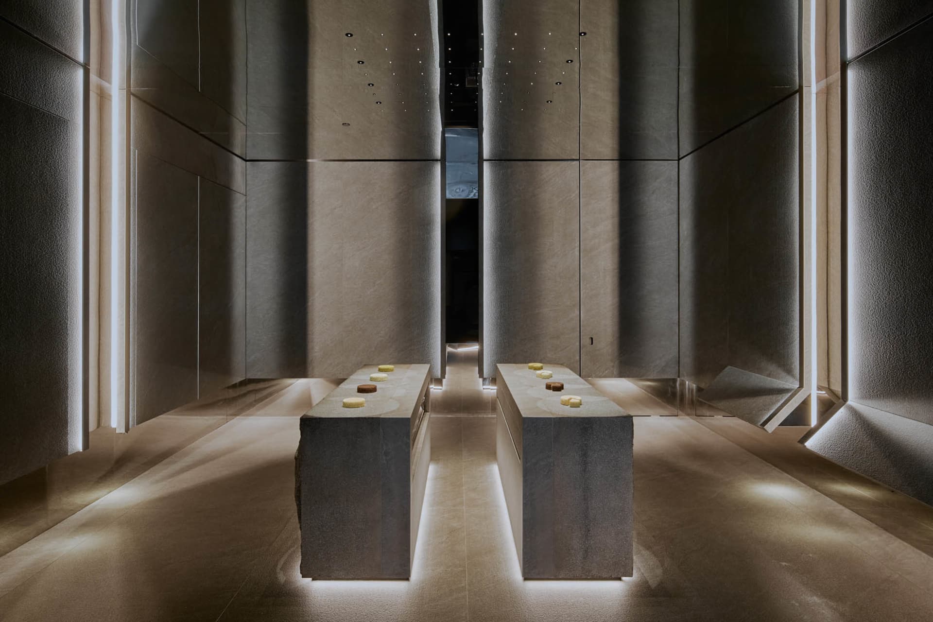 A dimly lit modern room with two stone tables and concrete walls and floors, creating a clean and minimalist atmosphere