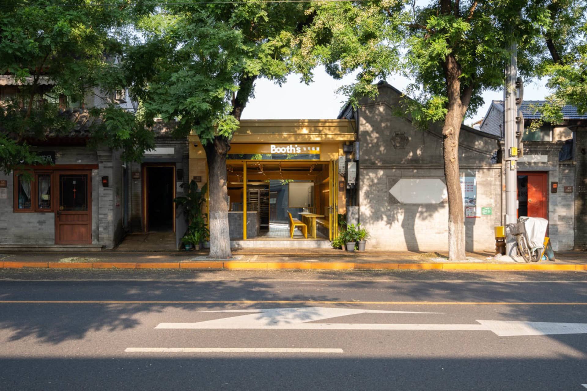 A building with a yellow doorway and a tree in front, surrounded by potted plants, giving a sense of urban design with a touch of nature