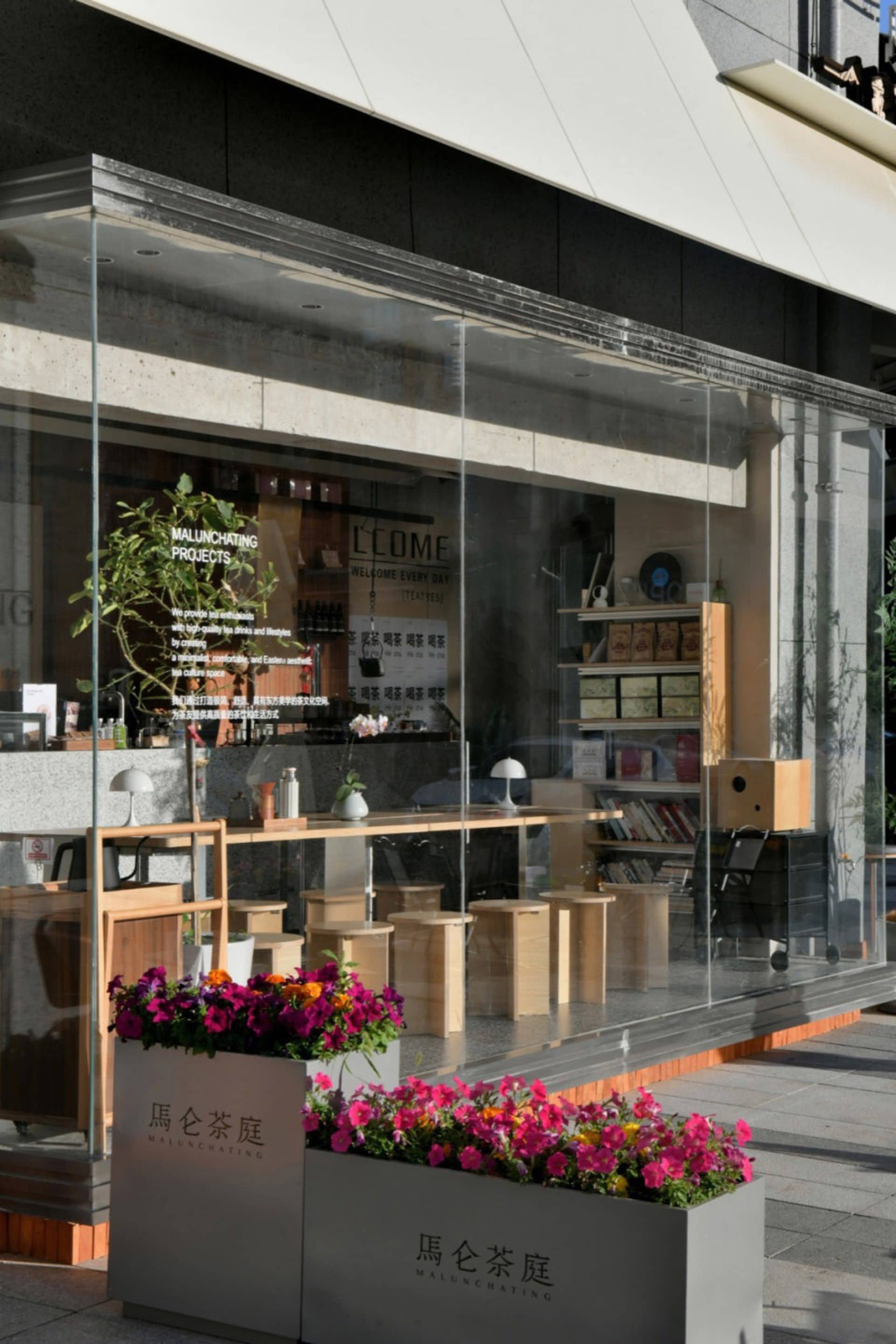 A welcoming retail space with a glass front, featuring potted plants, bottles, and chairs, creating a comfortable shopping environment