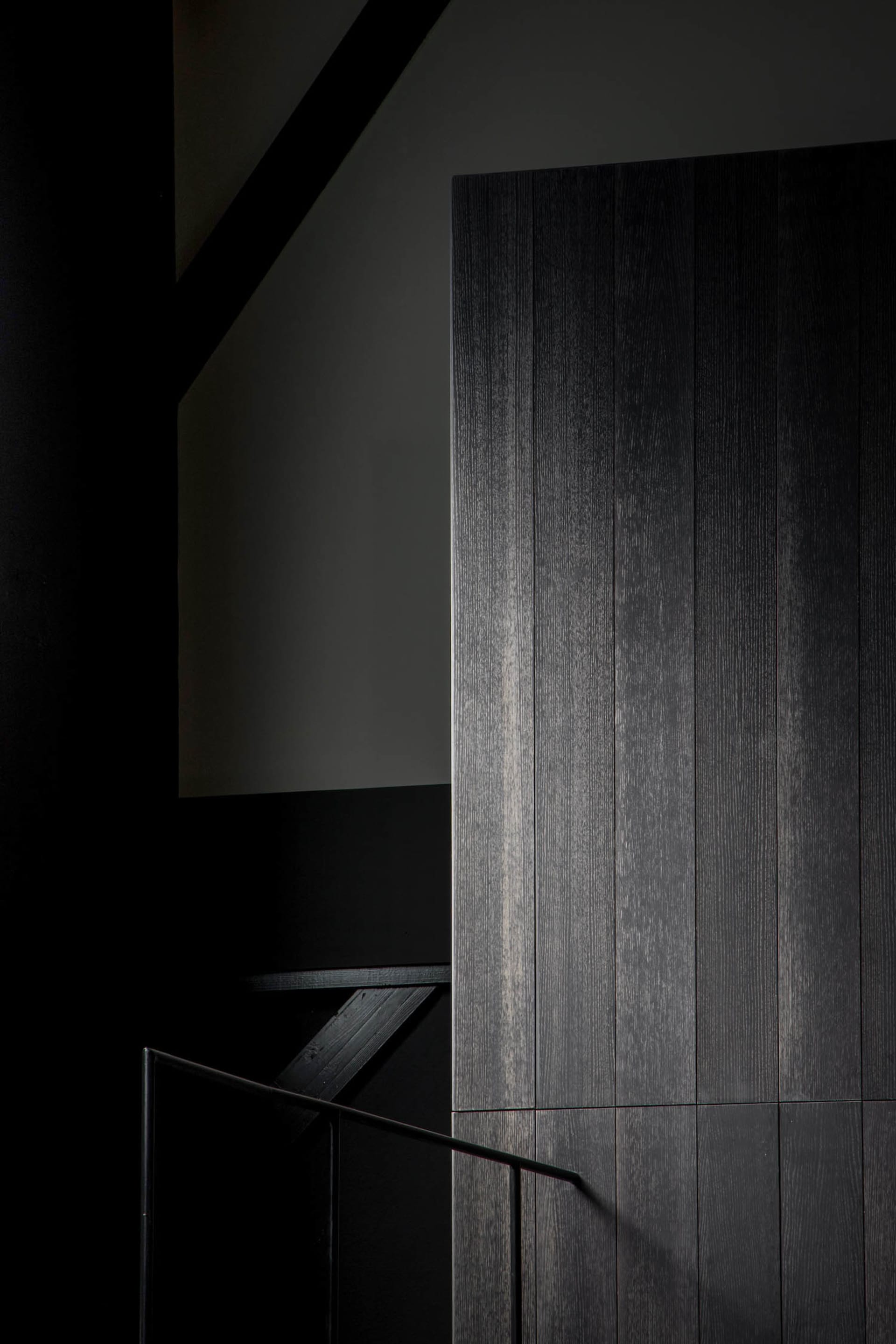 A modern interior space with a staircase made of wood, black walls, and a doorway leading to another level