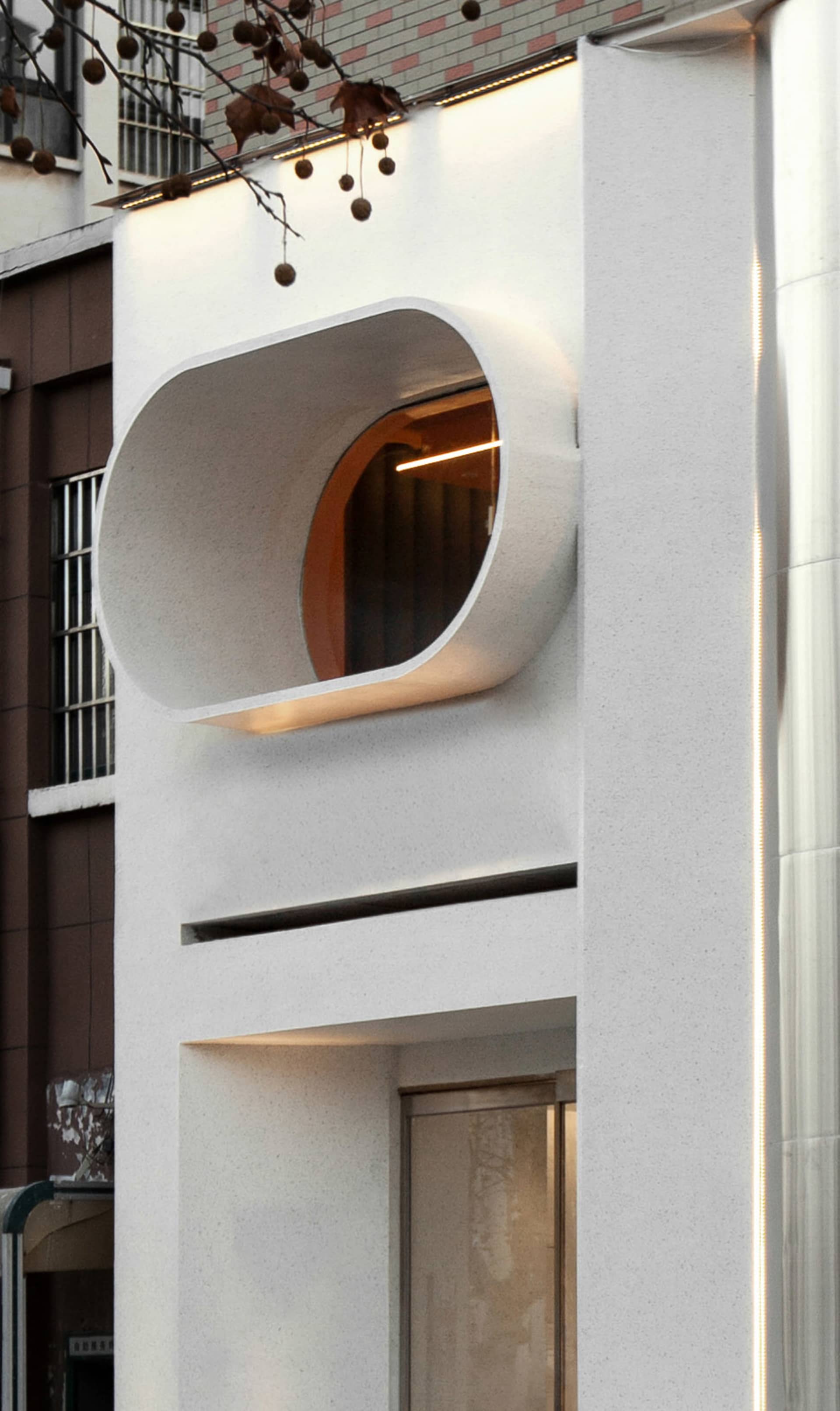 A modern building facade with a large white concrete wall featuring a round window, set against a neutral background