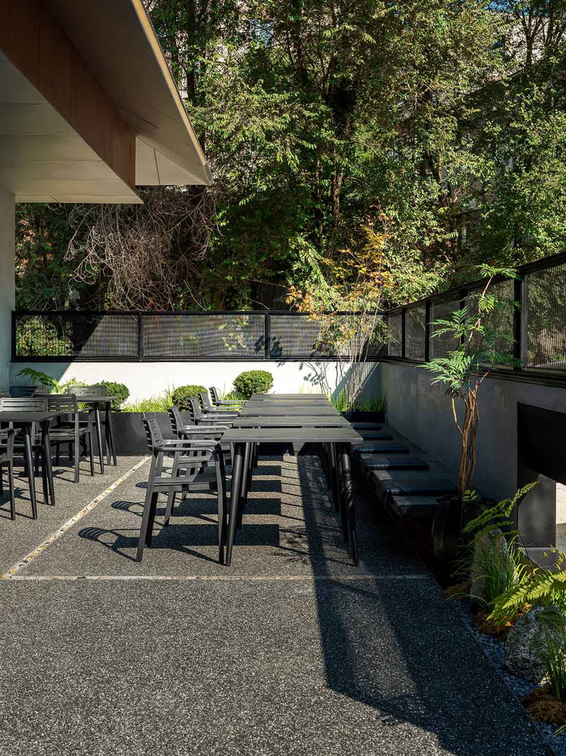 A relaxing outdoor patio area with black chairs and a dining table surrounded by potted plants