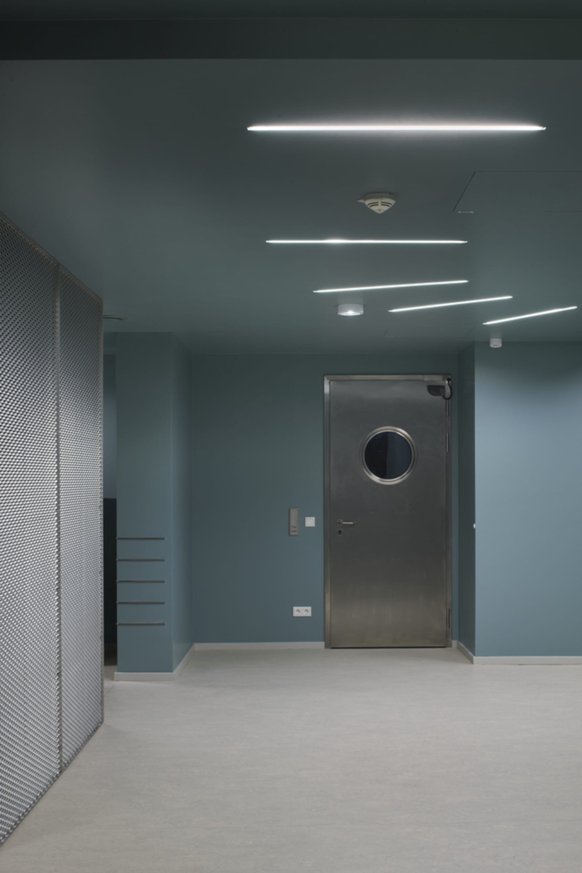 Industrial hallway with a blue wall, metal surfaces, and a door leading to another room