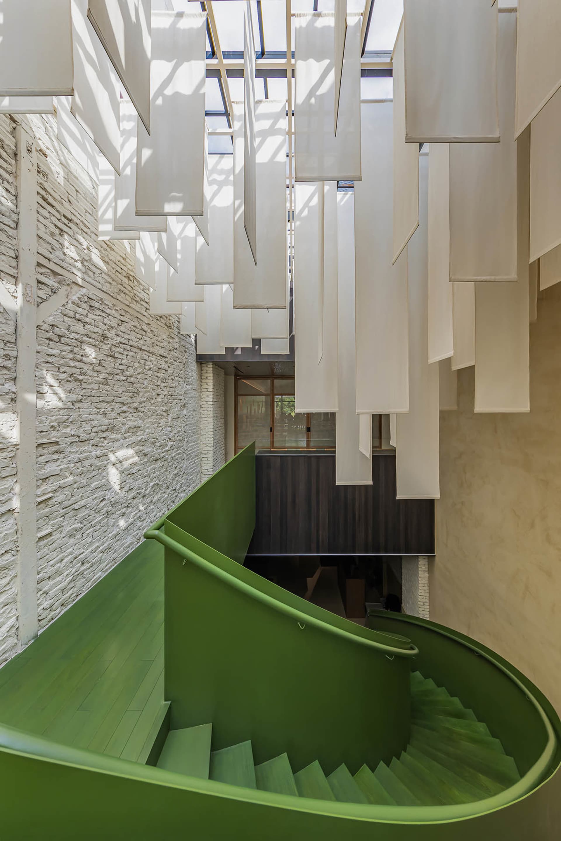 A museum staircase with white walls, green steps, and hanging white curtains creating a unique atmosphere with a sense of mystery or artistic expression
