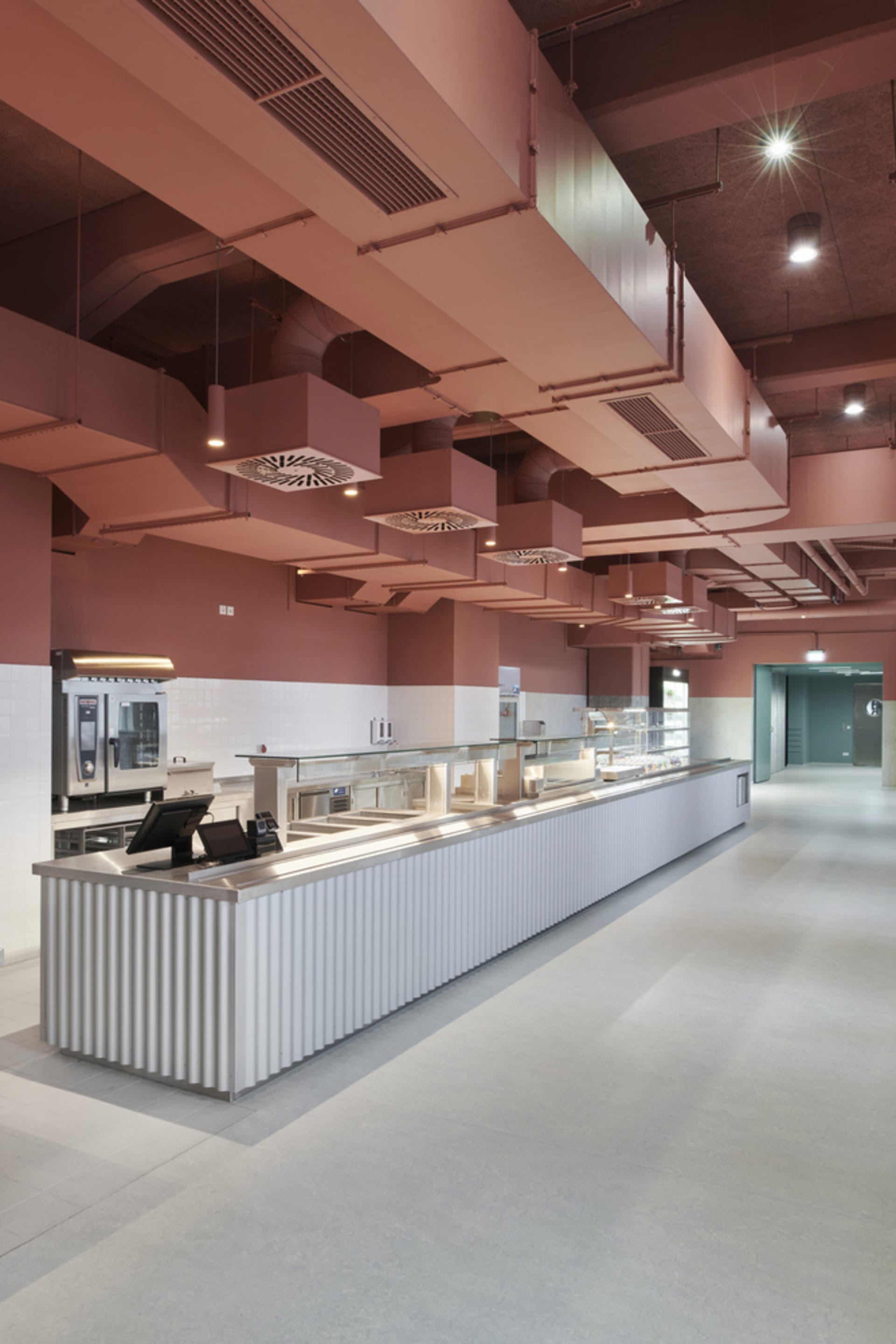 Modern restaurant kitchen with a counter, sink, cabinets, refrigerator, and ovens, featuring neutral tones and a clean atmosphere