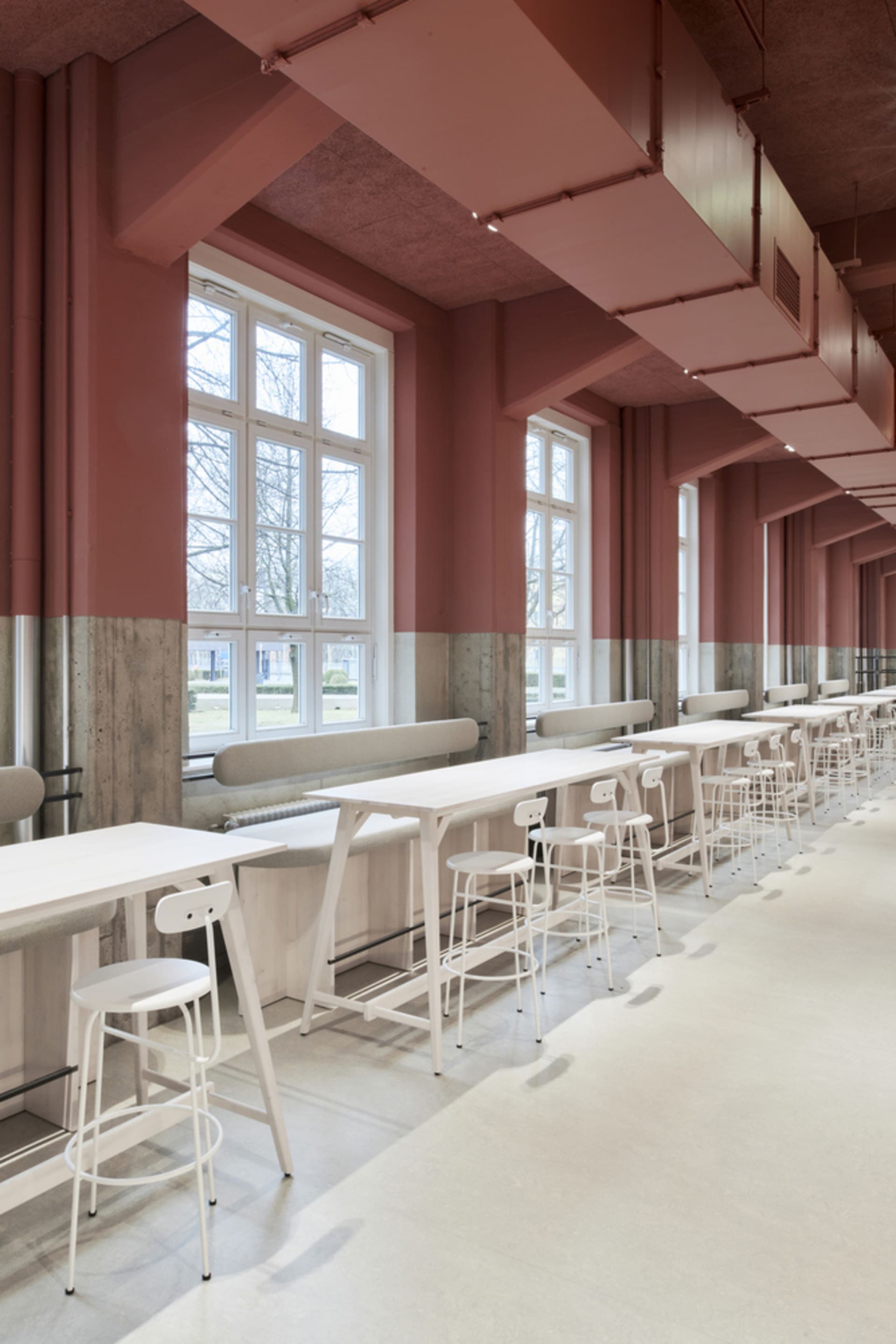 A modern dining space with pink walls, multiple tables, chairs, and benches, featuring a contemporary design with clean lines and minimalistic decoration
