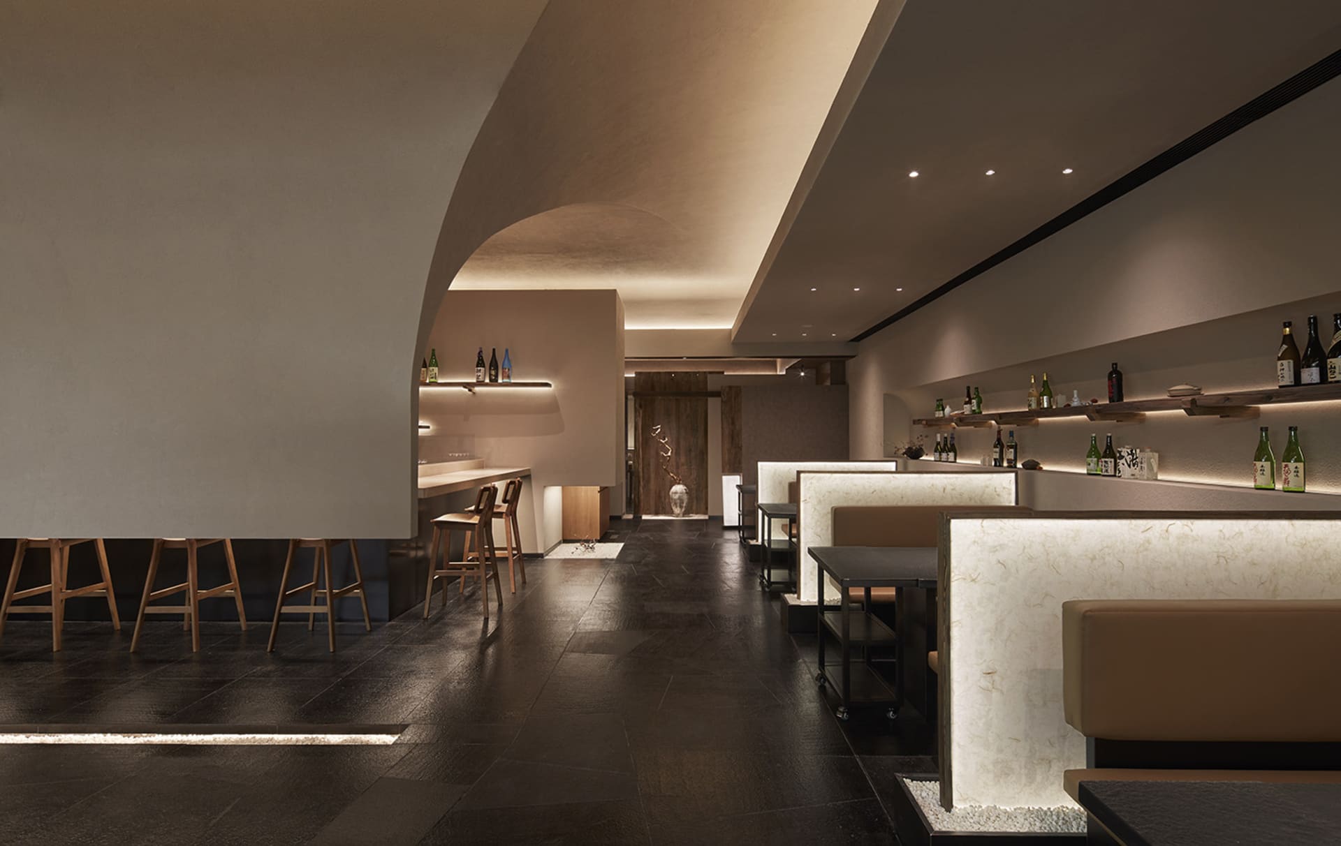 Modern restaurant interior with high ceilings, multiple dining tables, and modern wall design, featuring bottles and comfortable seating for guests