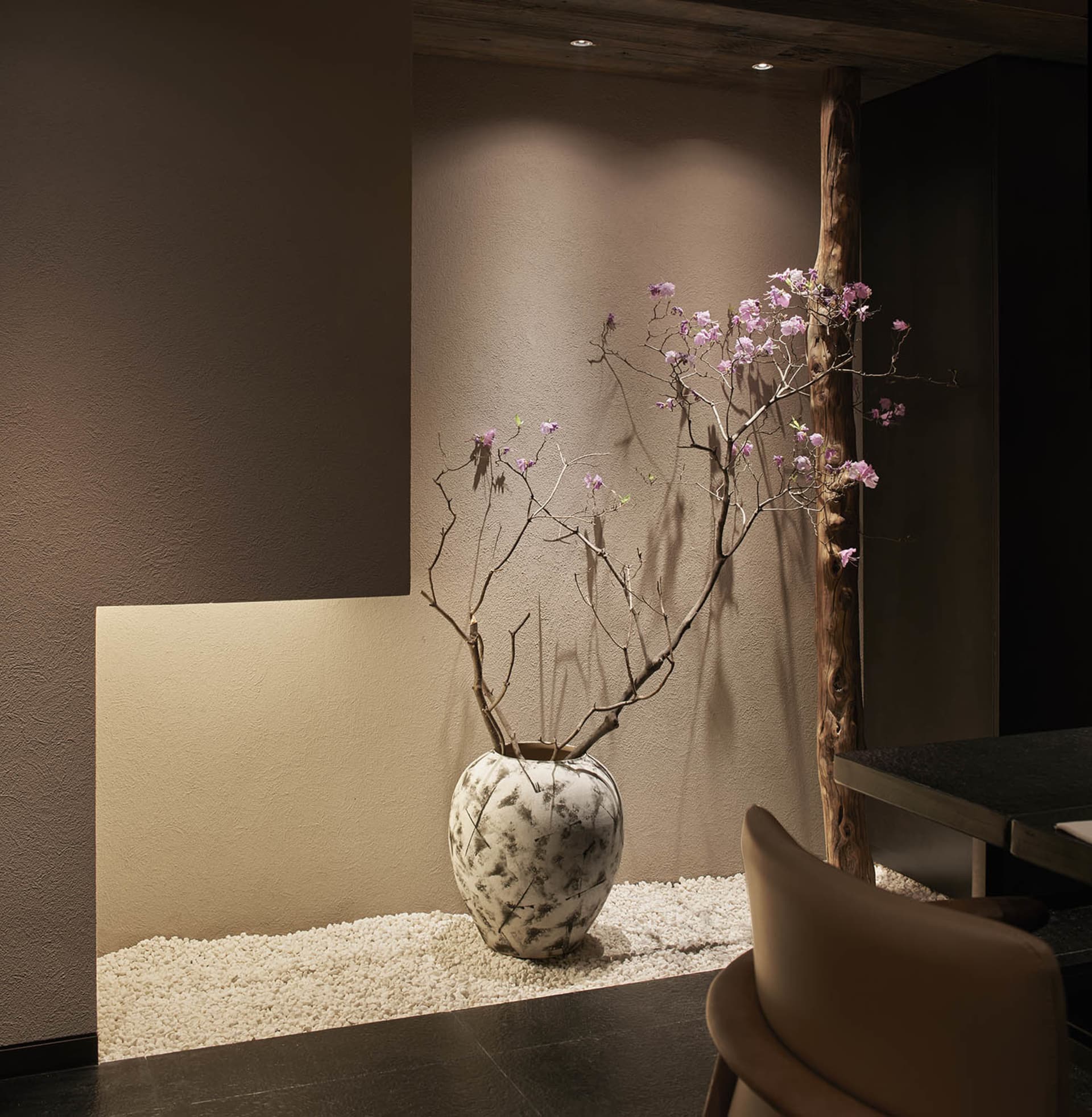 A cozy living space with a stone vase, two chairs, and a dining table, creating a warm atmosphere
