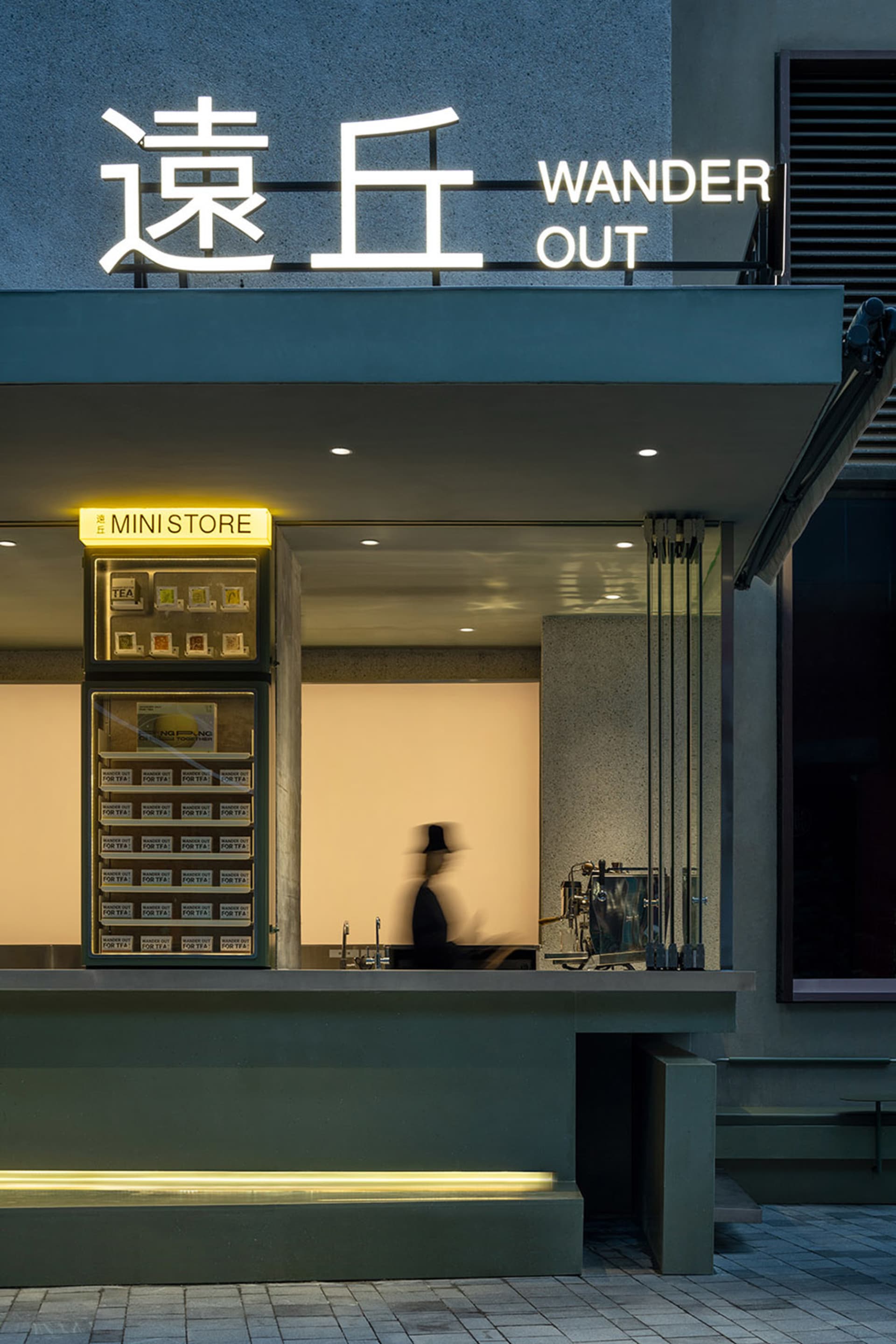A modern storefront with a glass front, visible interior, and a man walking past carrying a handbag in a lively urban environment