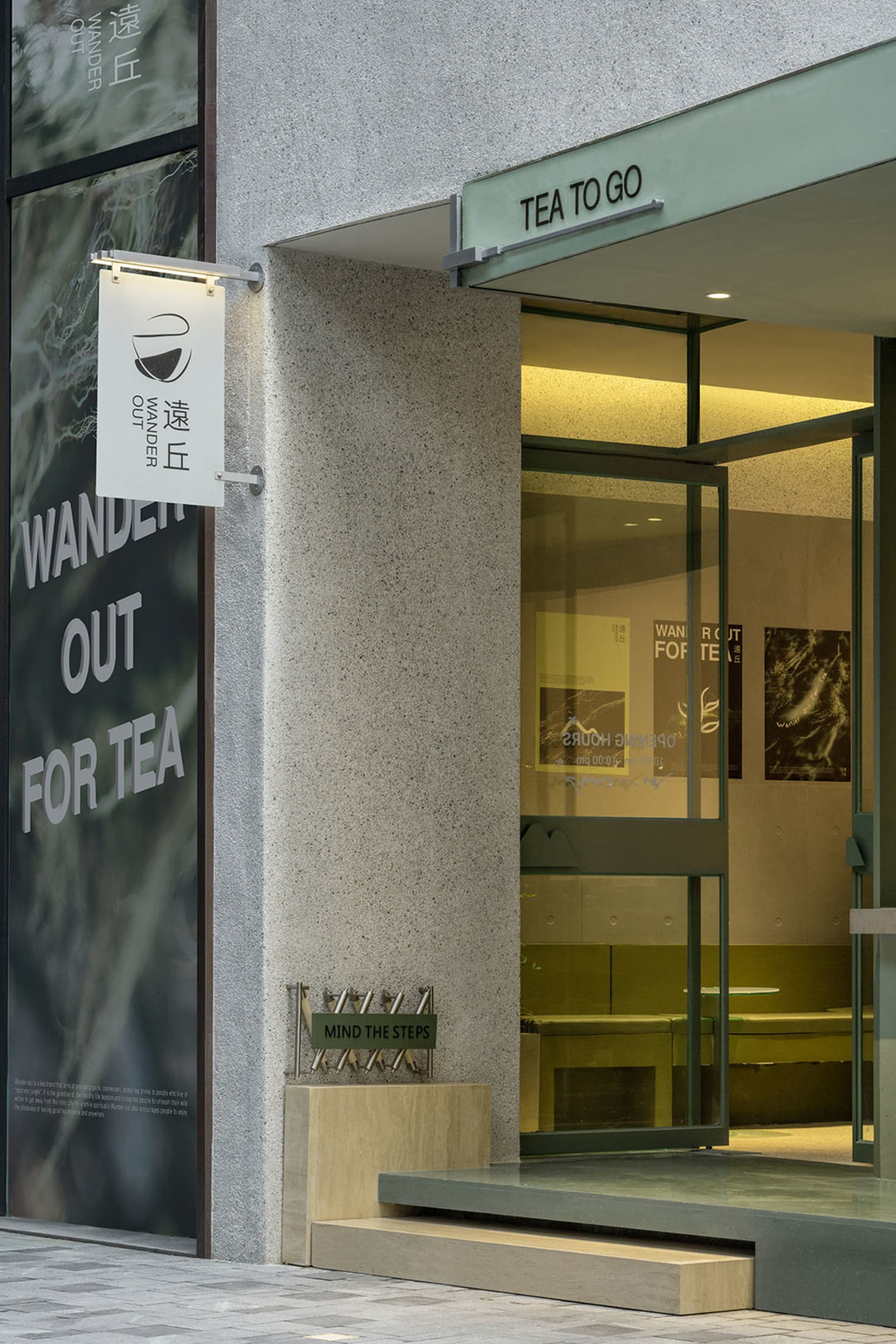 溫馨咖啡廳，白色牆面、灰石元素與玻璃門，門口招牌寫著「Wander Out For Tea」