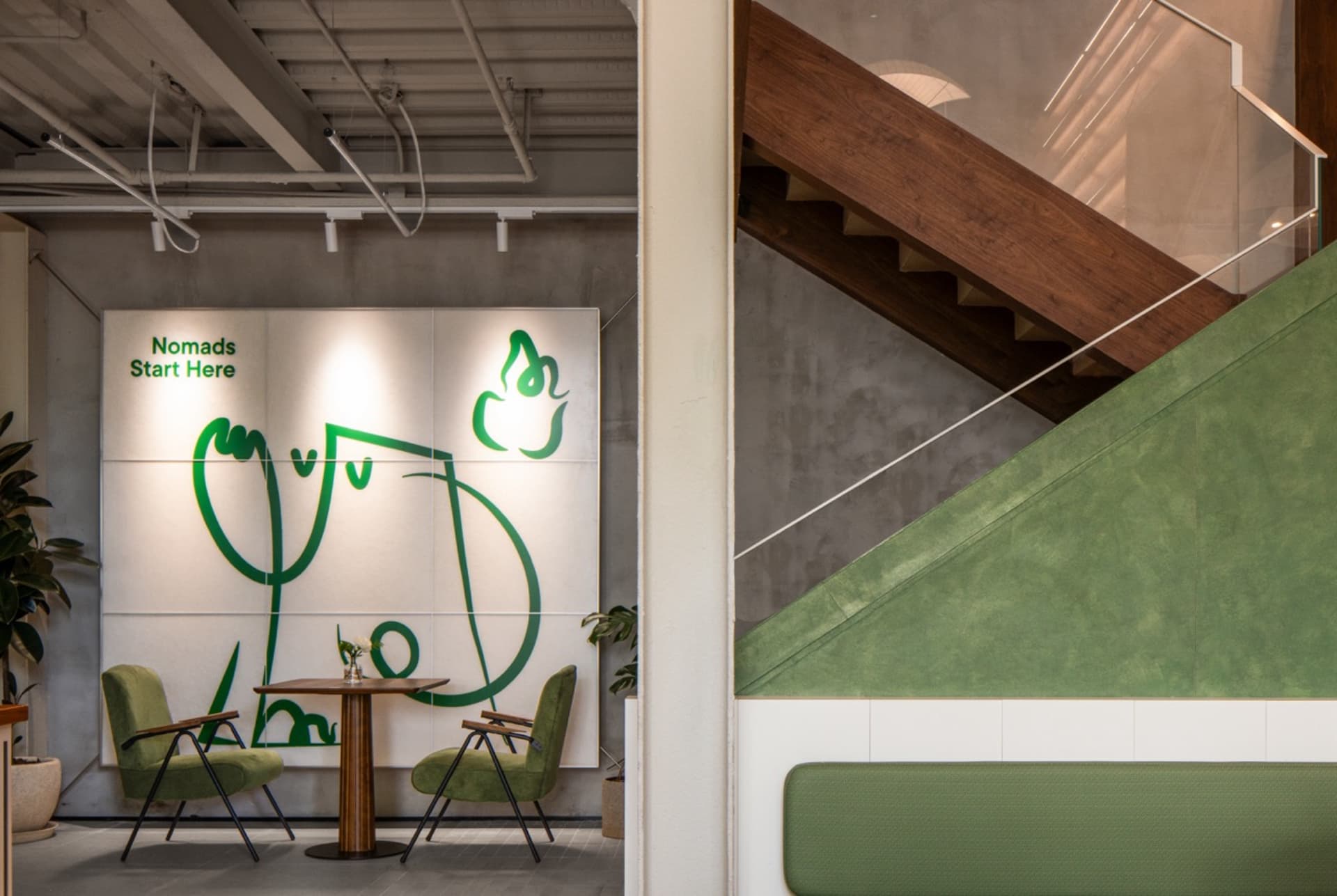 Industrial restaurant interior with green walls, wooden stairs, and dining tables with chairs, a potted plant adding greenery to the space