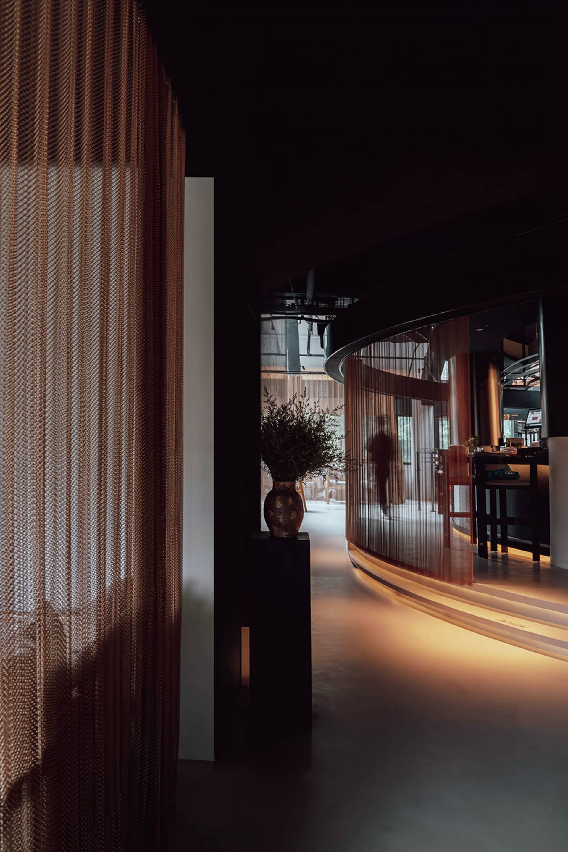 A black and white interior view of a restaurant or bar area with a curved wall, wood, and metal elements, featuring two people in conversation