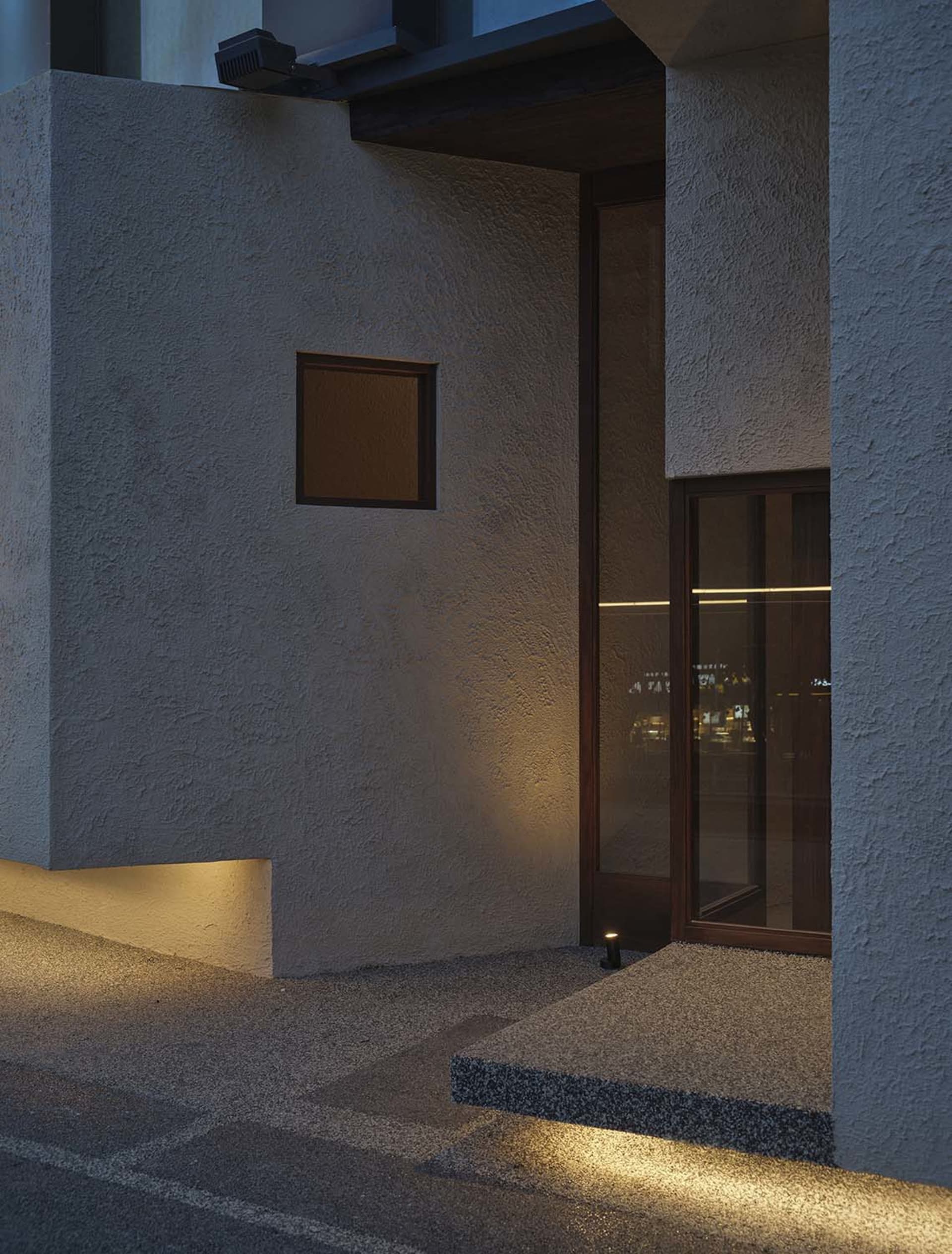 Exterior building facade with a doorway, two windows, and a window above the doorway, suggesting a sturdy concrete or similar material construction